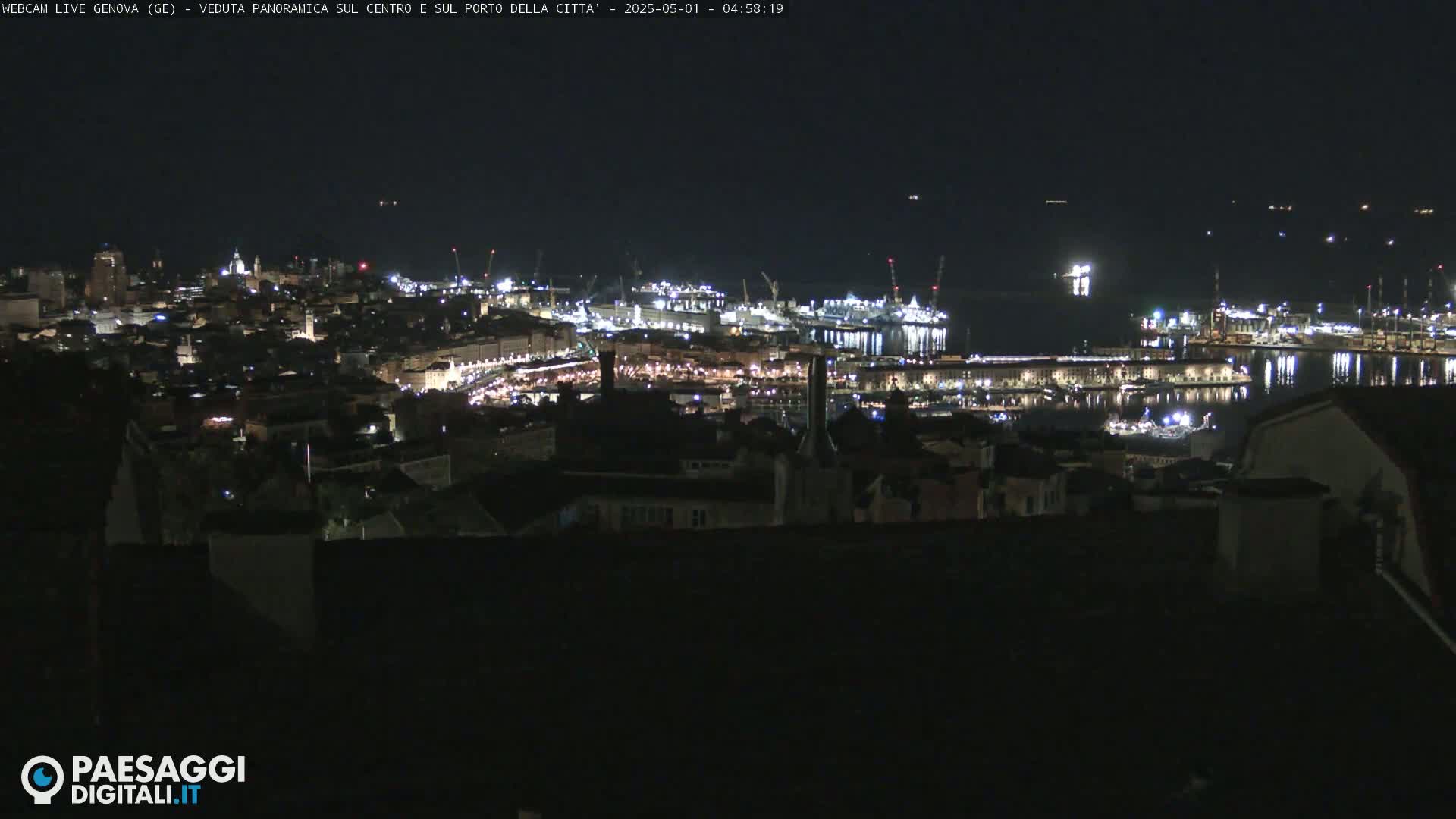 A nighttime, panoramic view of a city's illuminated harbor and buildings, extending to a dark body of water.