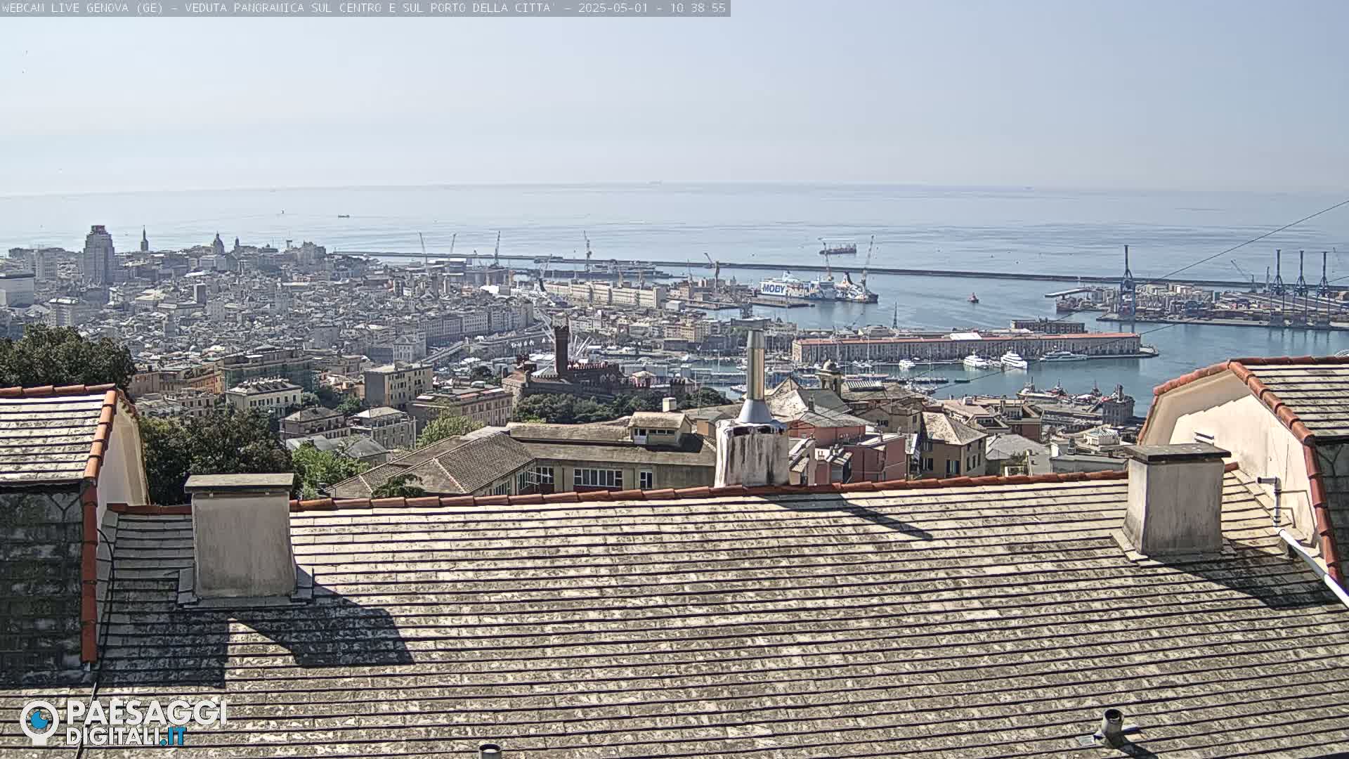 A panoramic view of a city harbor and cityscape on a sunny day, seen from a rooftop with a tiled roof.