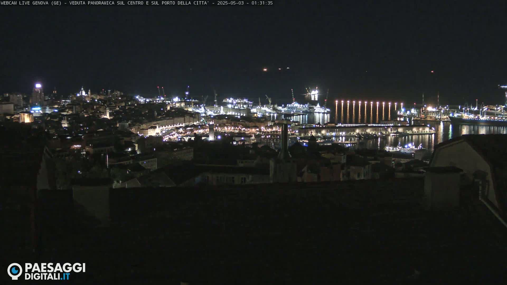 A nighttime, panoramic view of a city's harbor and illuminated cityscape, with calm water reflecting the lights.