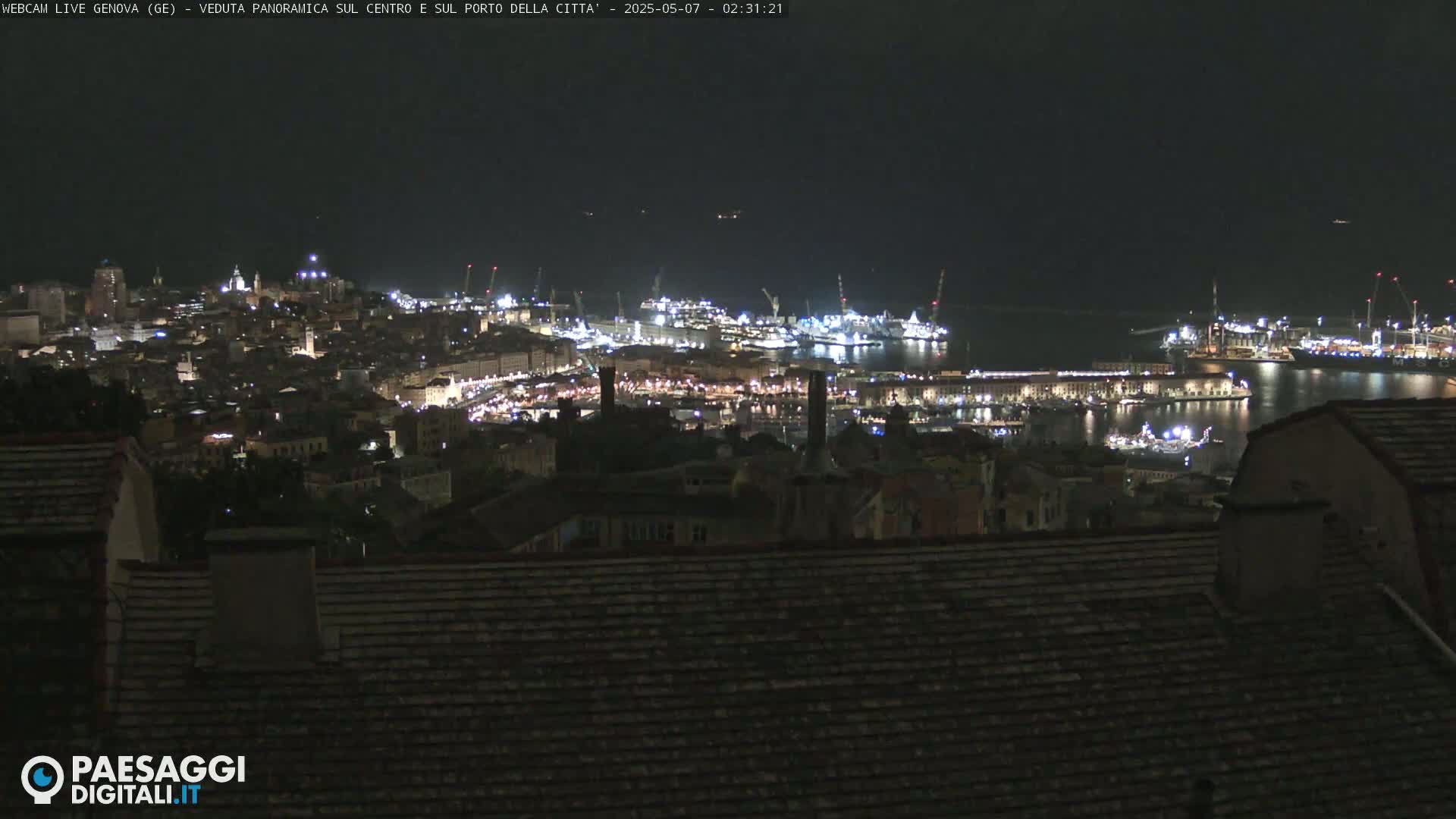 A nighttime, panoramic view of a city harbor with many lights, under a clear, dark sky.