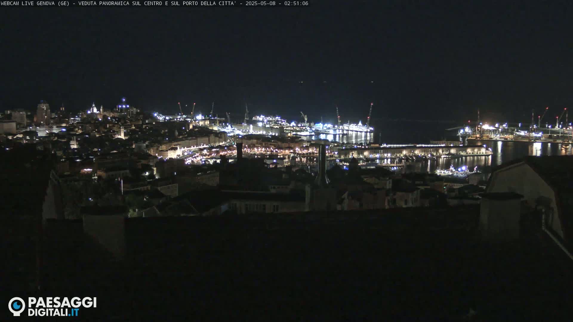 A nighttime panoramic view of a city's illuminated harbor and buildings, under a clear, dark sky.