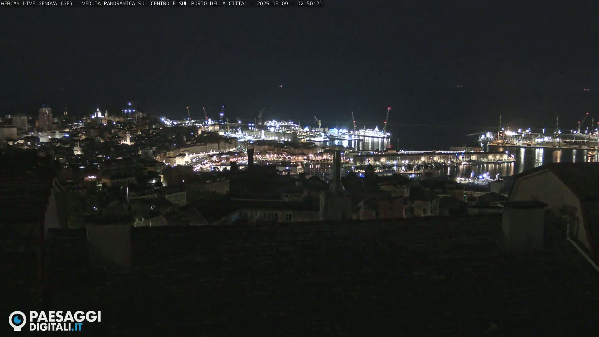 A nighttime panoramic view of a city's harbor and illuminated buildings, extending to the dark waters beyond.