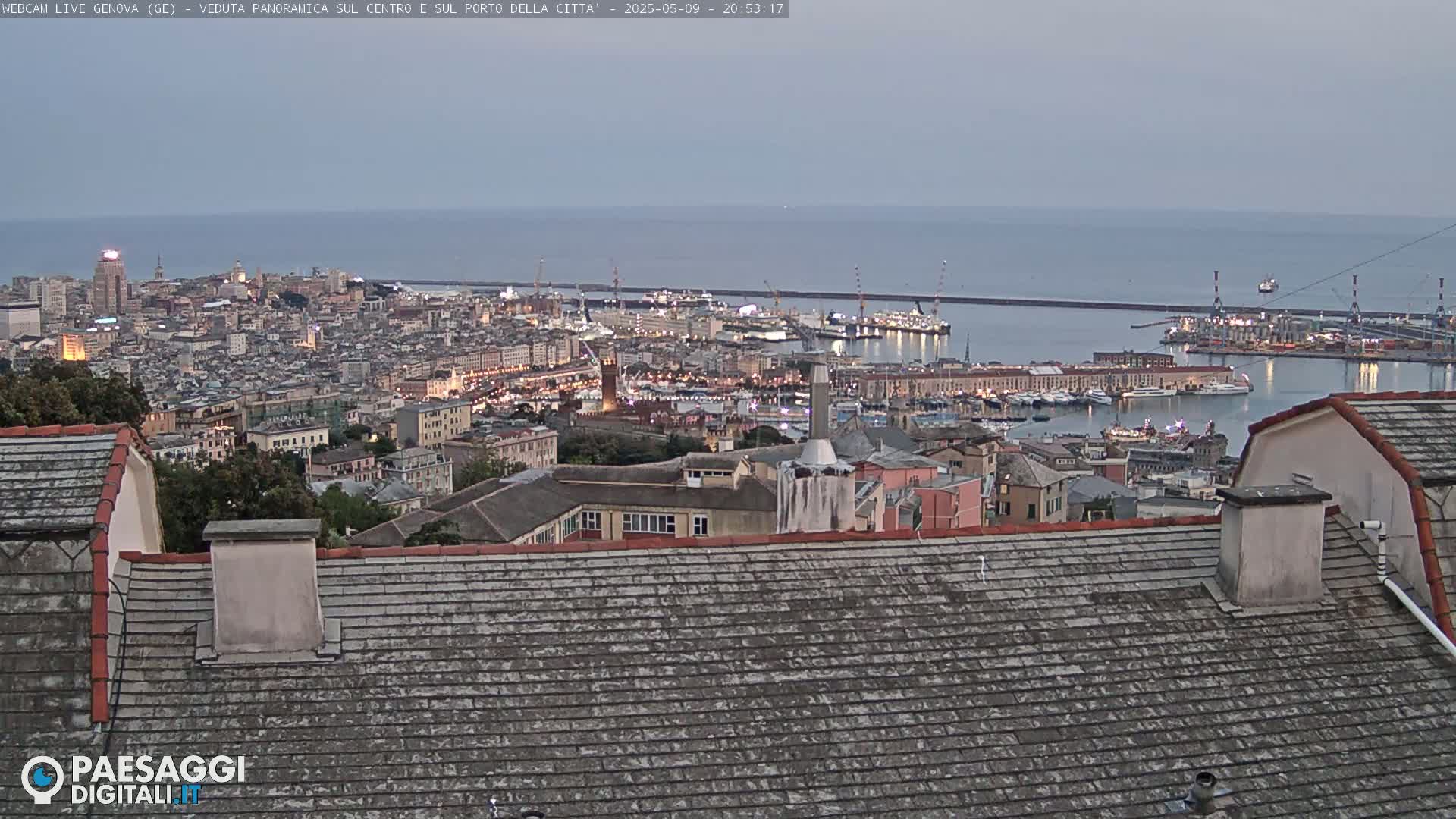 A twilight view of a city and its harbor, extending to a calm sea under a dusky sky.