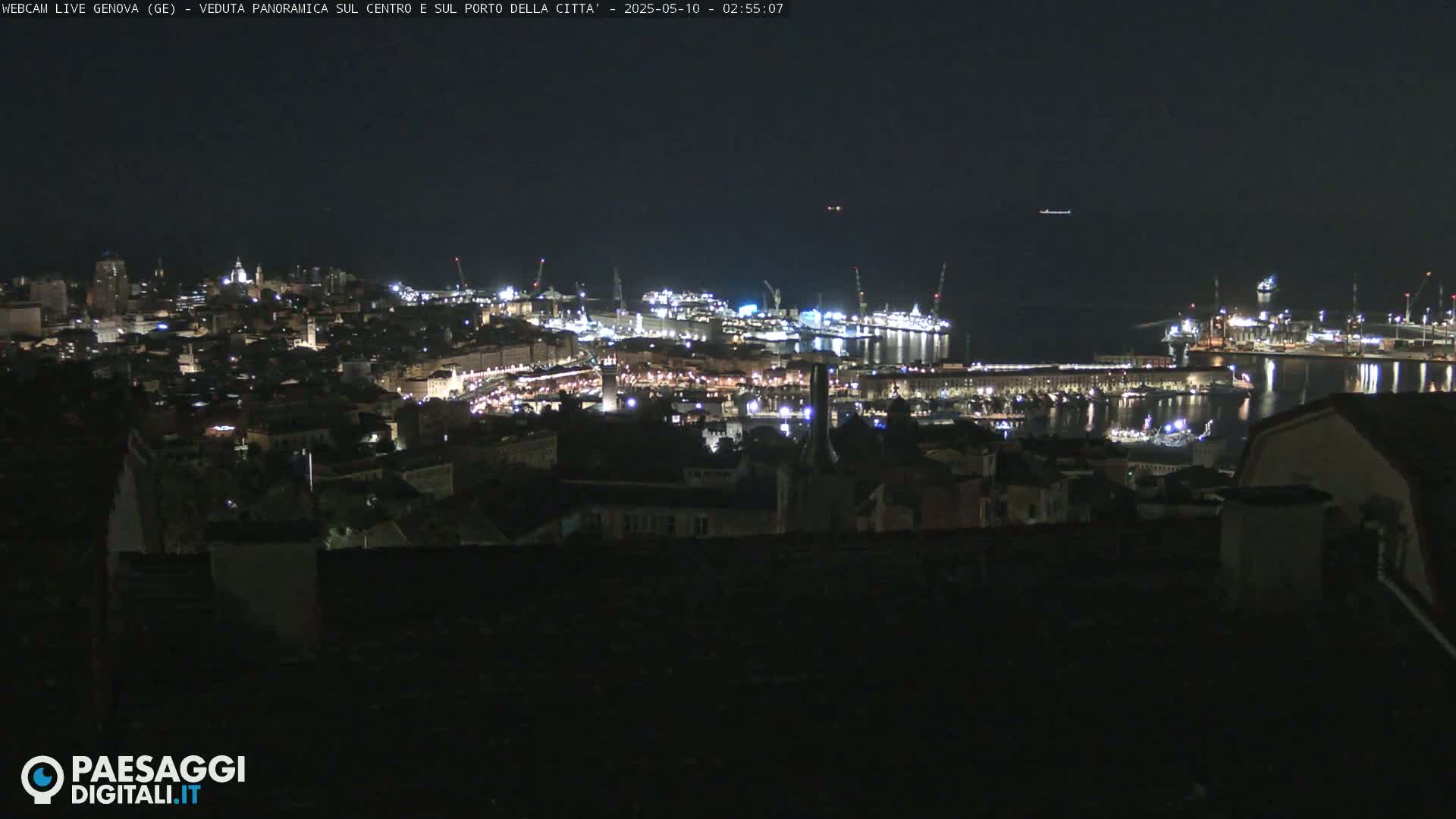 A nighttime panoramic view of a city's harbor and illuminated cityscape, with calm water reflecting the lights.