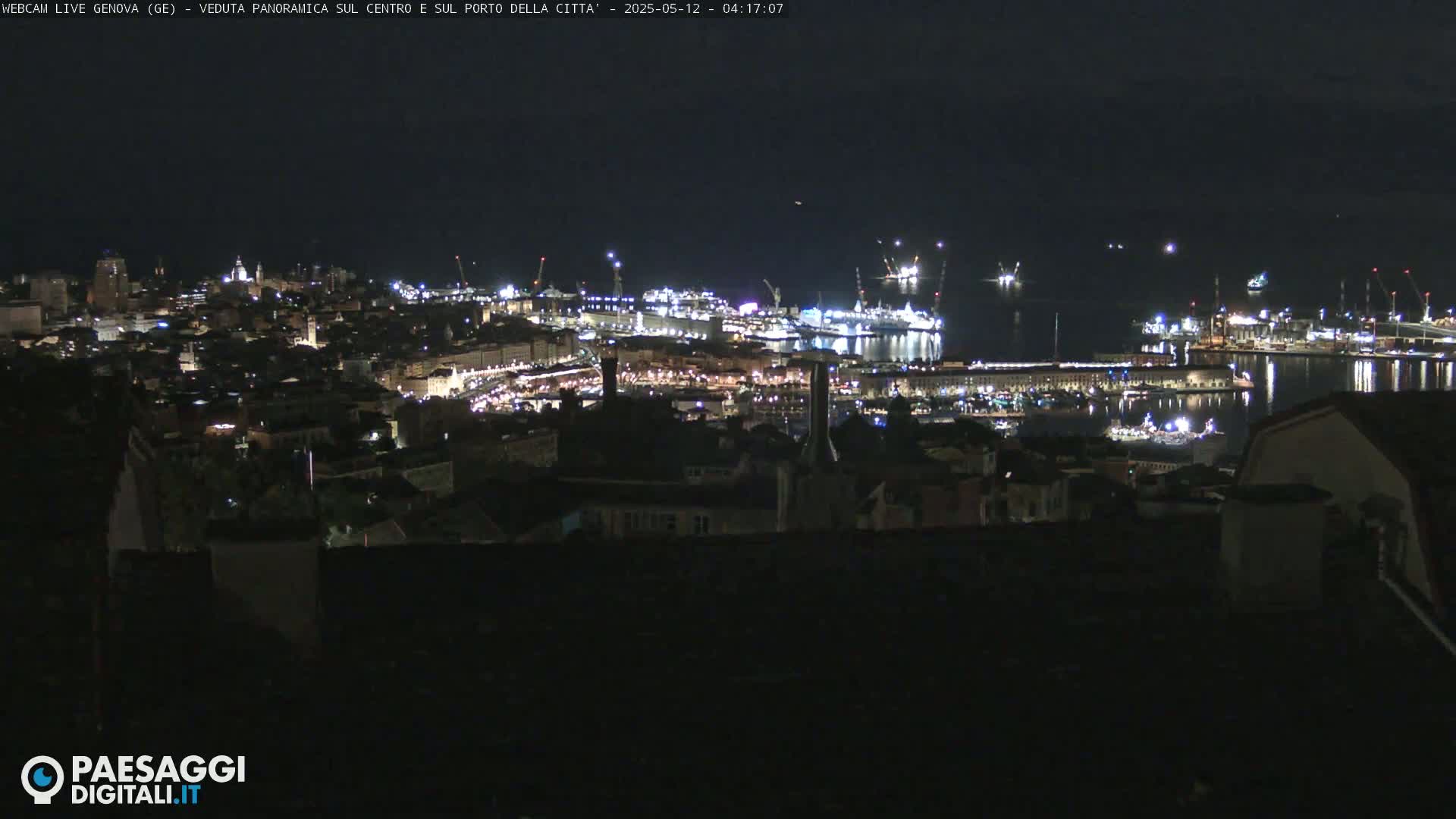 A nighttime panoramic view of a city's harbor and illuminated cityscape.