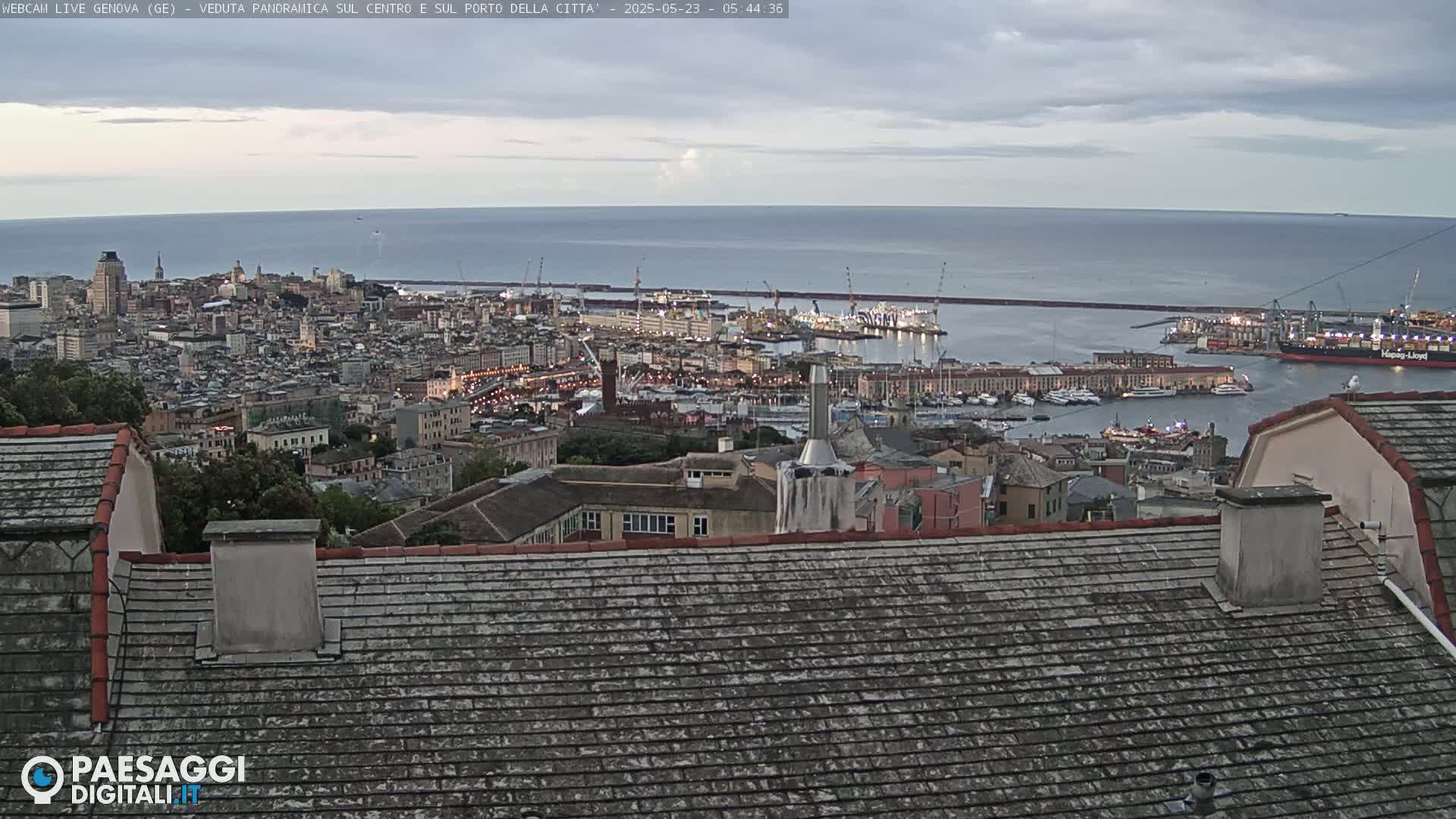 A panoramic view of a city and harbor on a cloudy day, overlooking a calm sea.