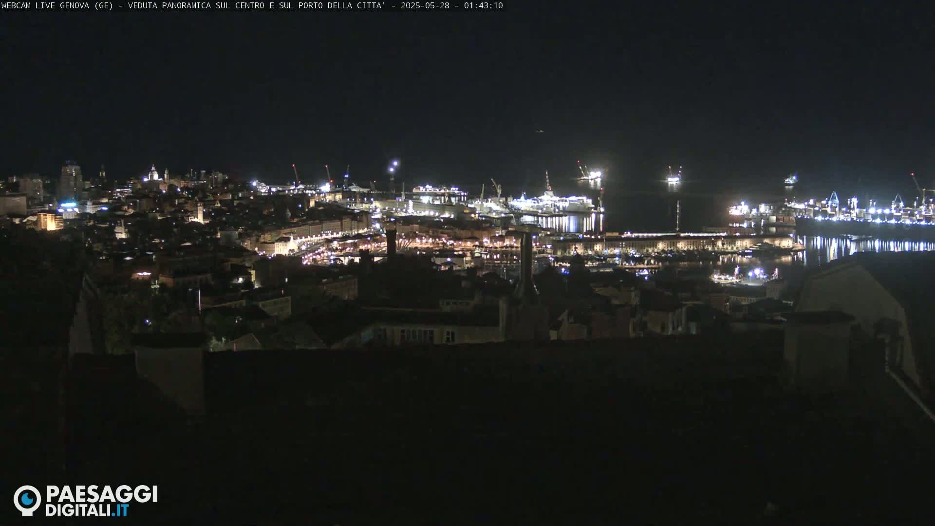 A nighttime, panoramic view of a city's harbor and illuminated cityscape, showing numerous ships and buildings under a clear, dark sky.