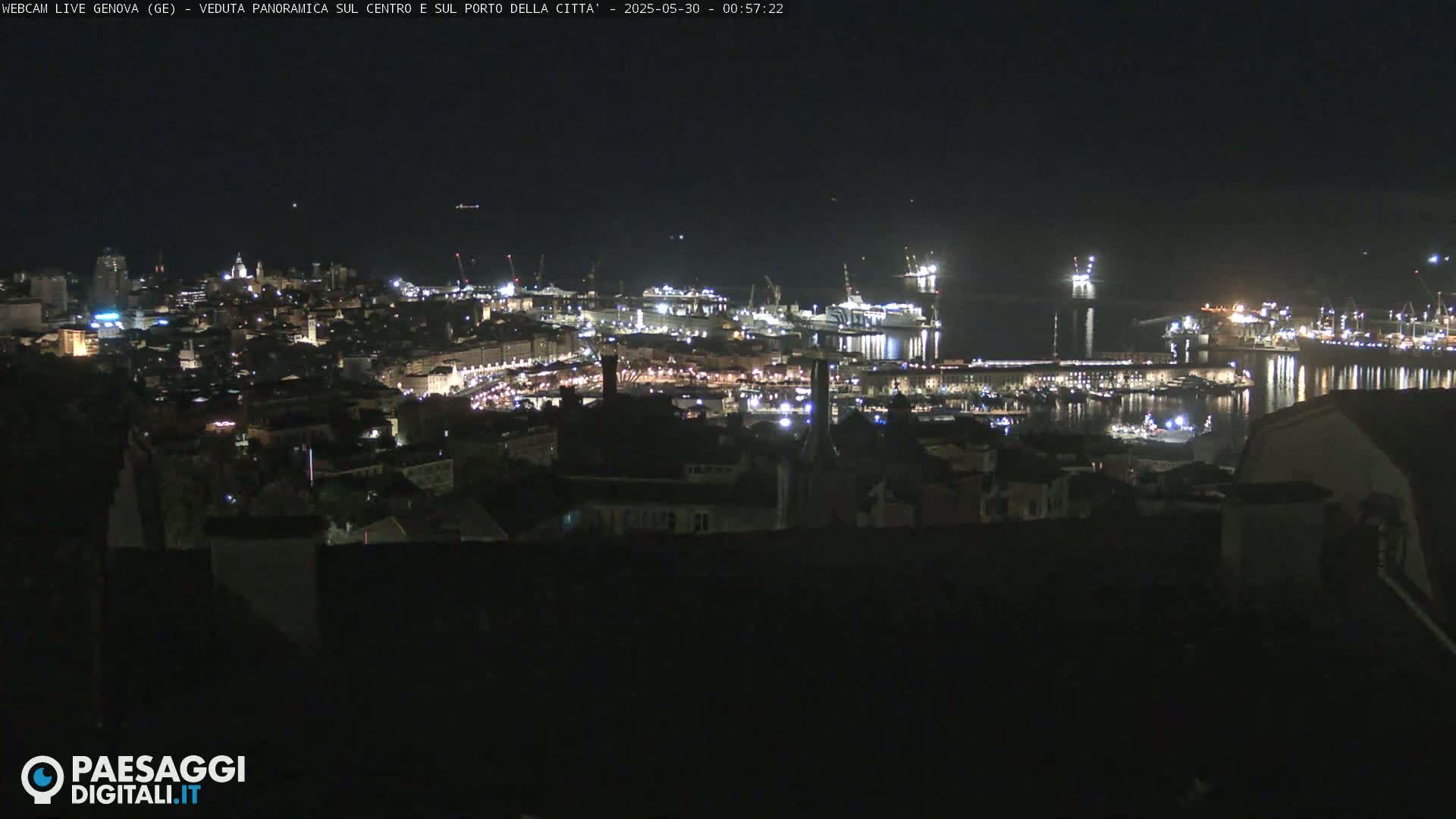 A nighttime panoramic view of a city's illuminated harbor and buildings under a clear, dark sky.