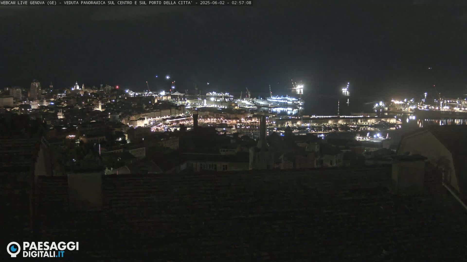 A nighttime, panoramic view of a city's harbor and illuminated cityscape, with calm waters.