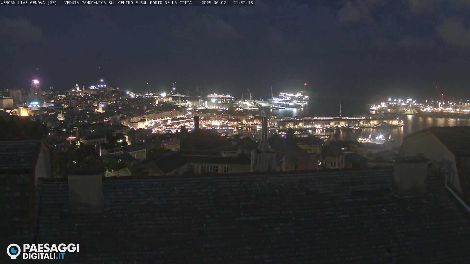 A nighttime, panoramic view of a city's harbor and illuminated cityscape under a dark sky.