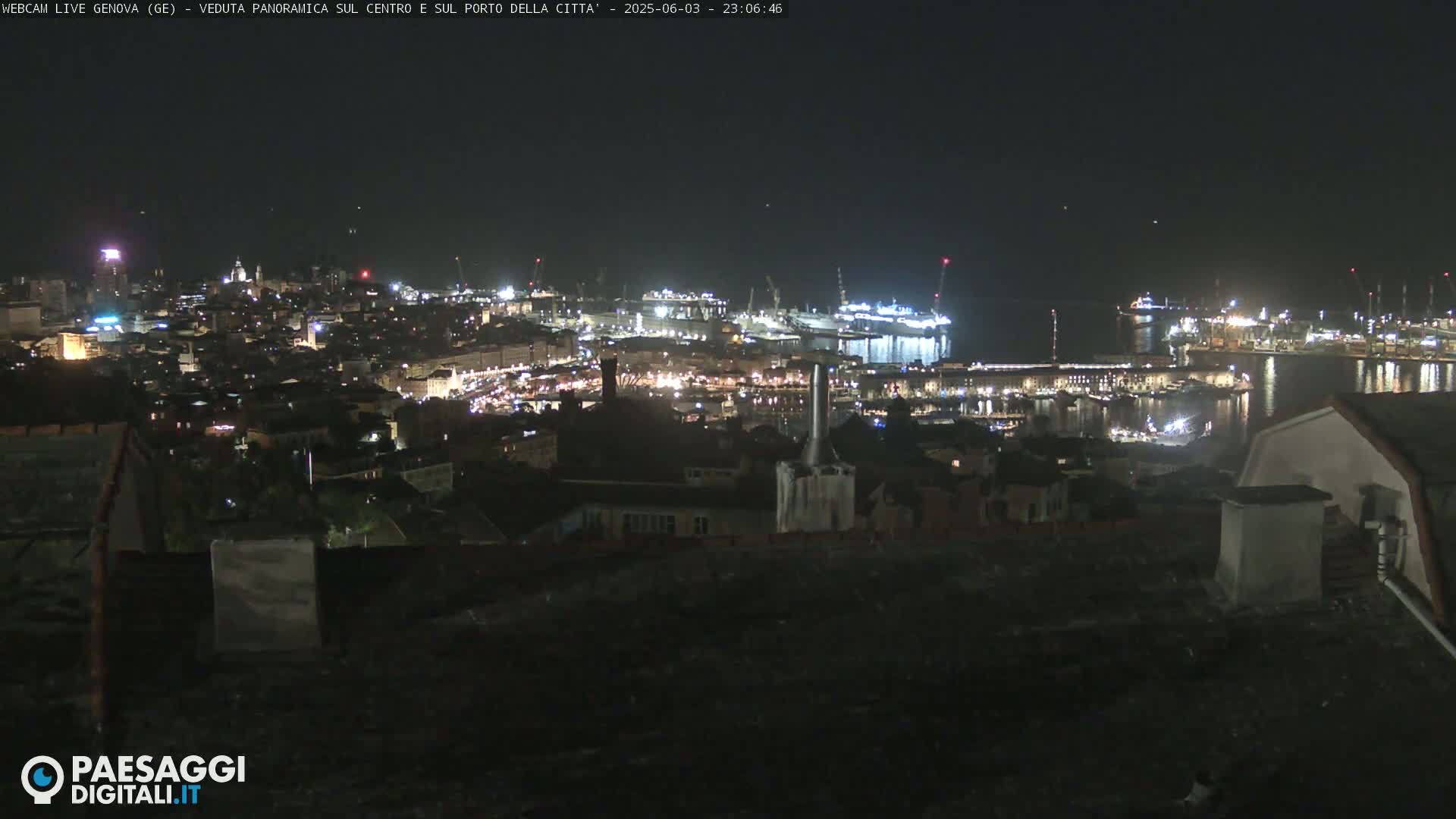 A nighttime, panoramic view of a city and its harbor, illuminated by lights, under a clear, dark sky.