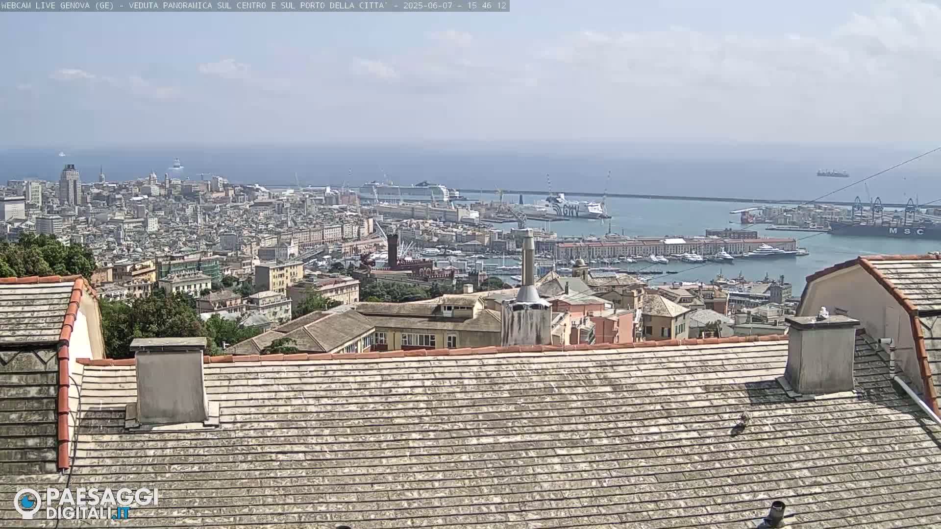 A panoramic view of a city and harbor on a partly sunny day, seen from a high vantage point with rooftops in the foreground.