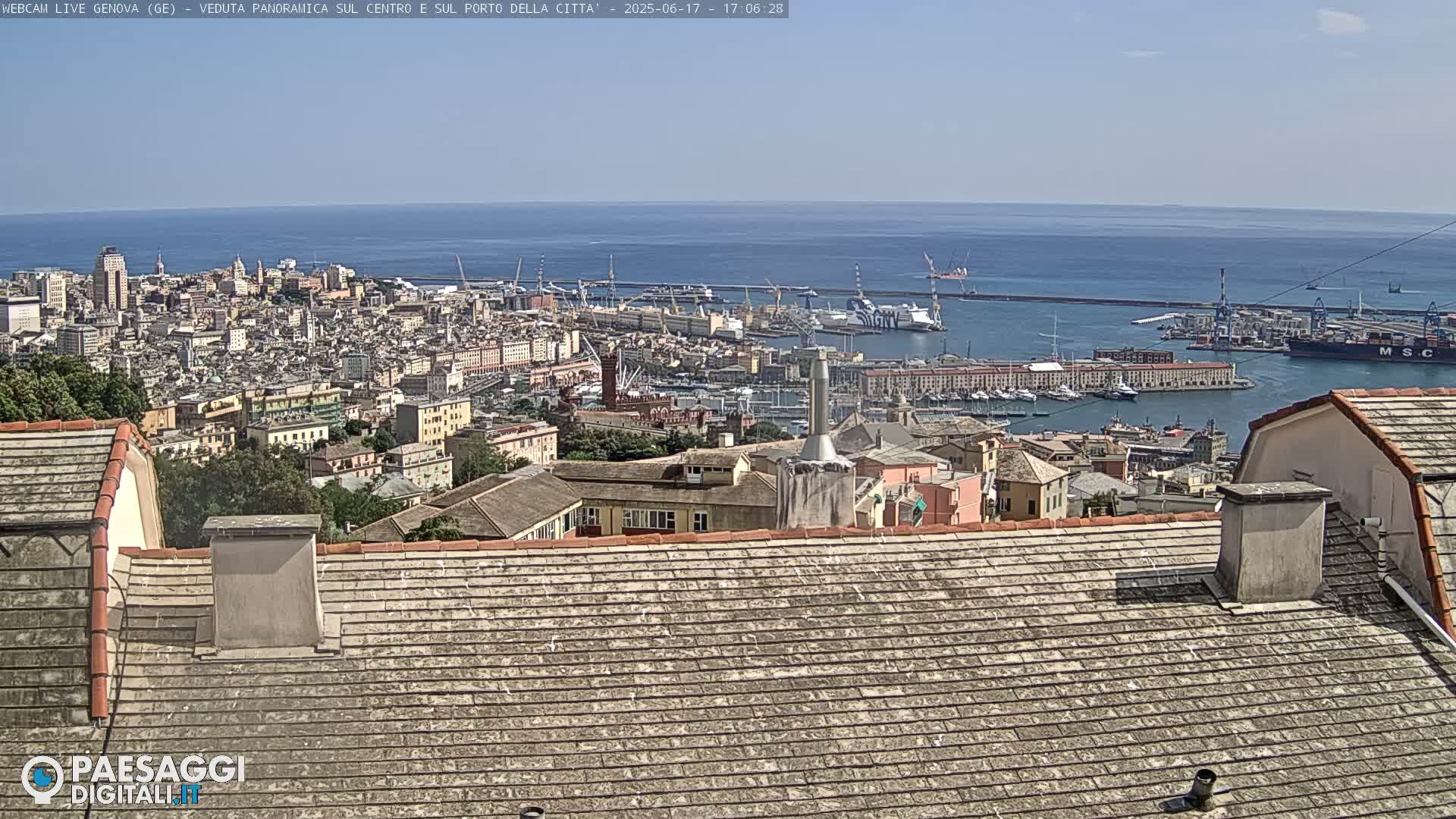 A panoramic view of a city and its harbor on a sunny day, seen from a rooftop.