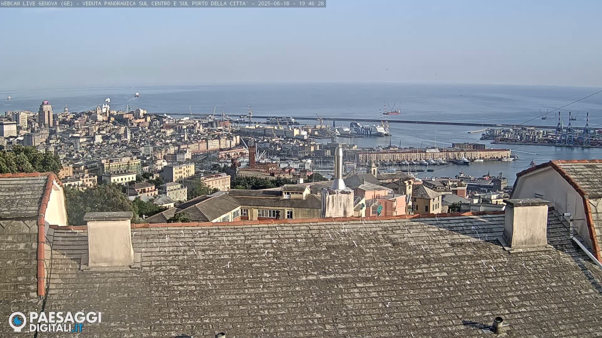 A panoramic view of a city and harbor on a clear day shows a large body of water, numerous buildings, and a busy port area.