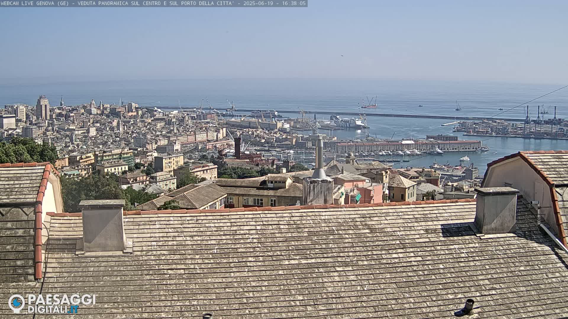 A panoramic view of a city and harbor on a sunny day, seen from a rooftop with weathered gray tiles.