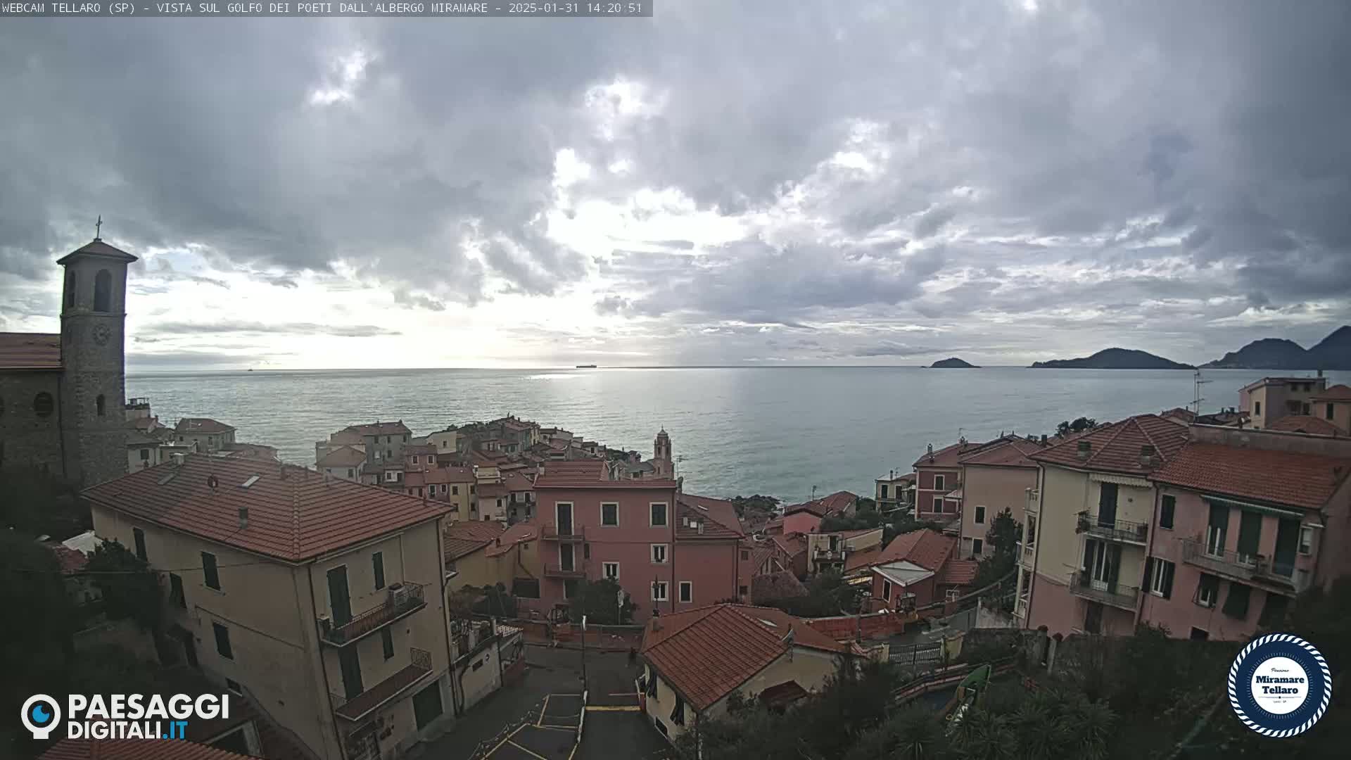 A coastal town with red-tiled roofs overlooks a calm sea under a mostly cloudy sky.