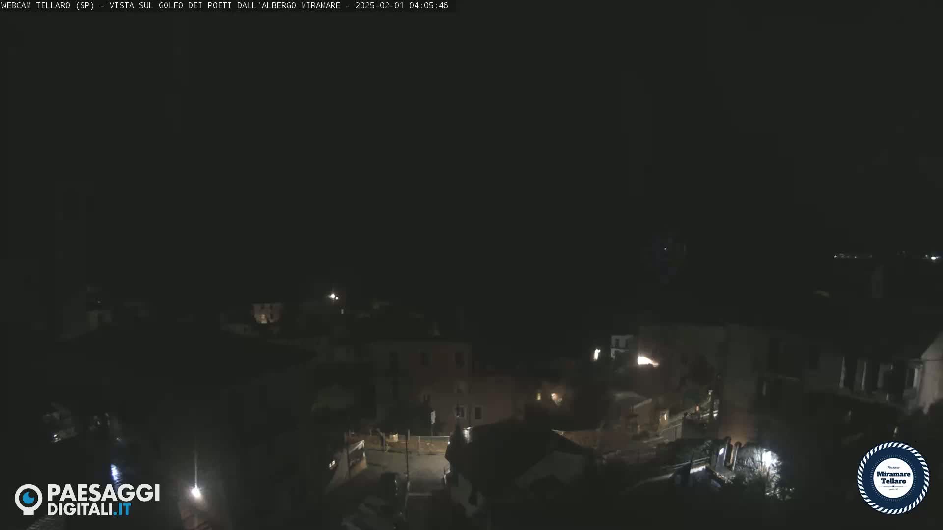 A nighttime, high-angle view of a dimly lit town, possibly coastal, under a dark sky.