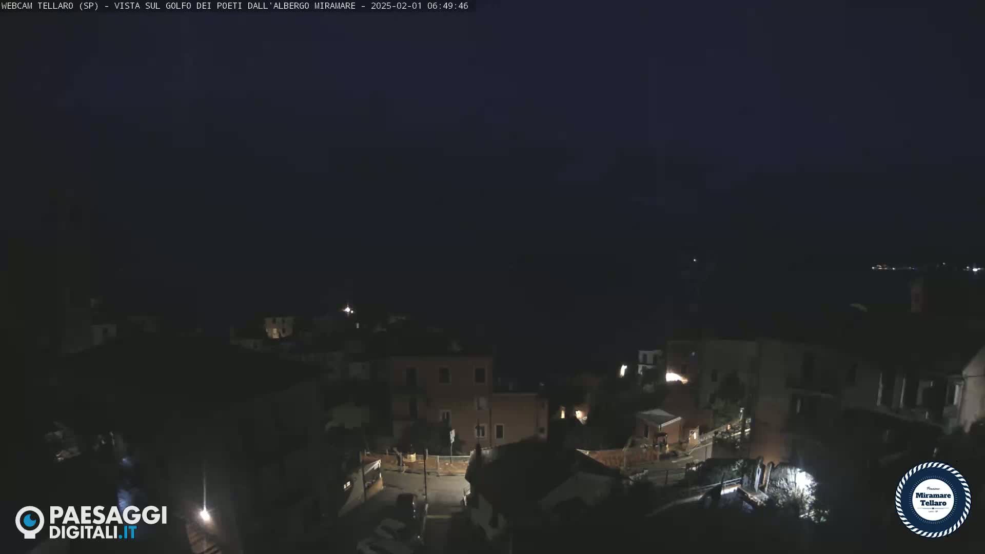 A nighttime, overhead view of a small town nestled along a dark coastline under a clear, dark sky.