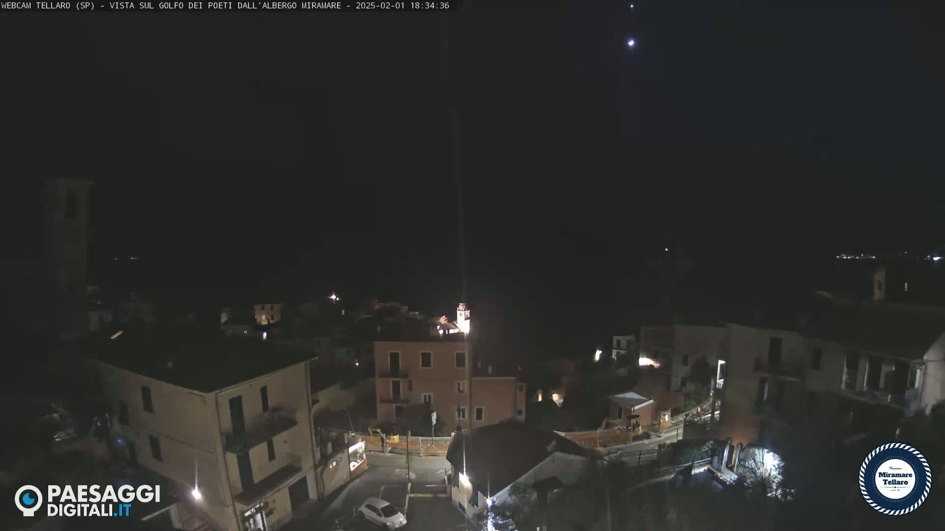 A nighttime aerial view of a small town with sparsely lit buildings under a clear, dark sky dotted with stars.
