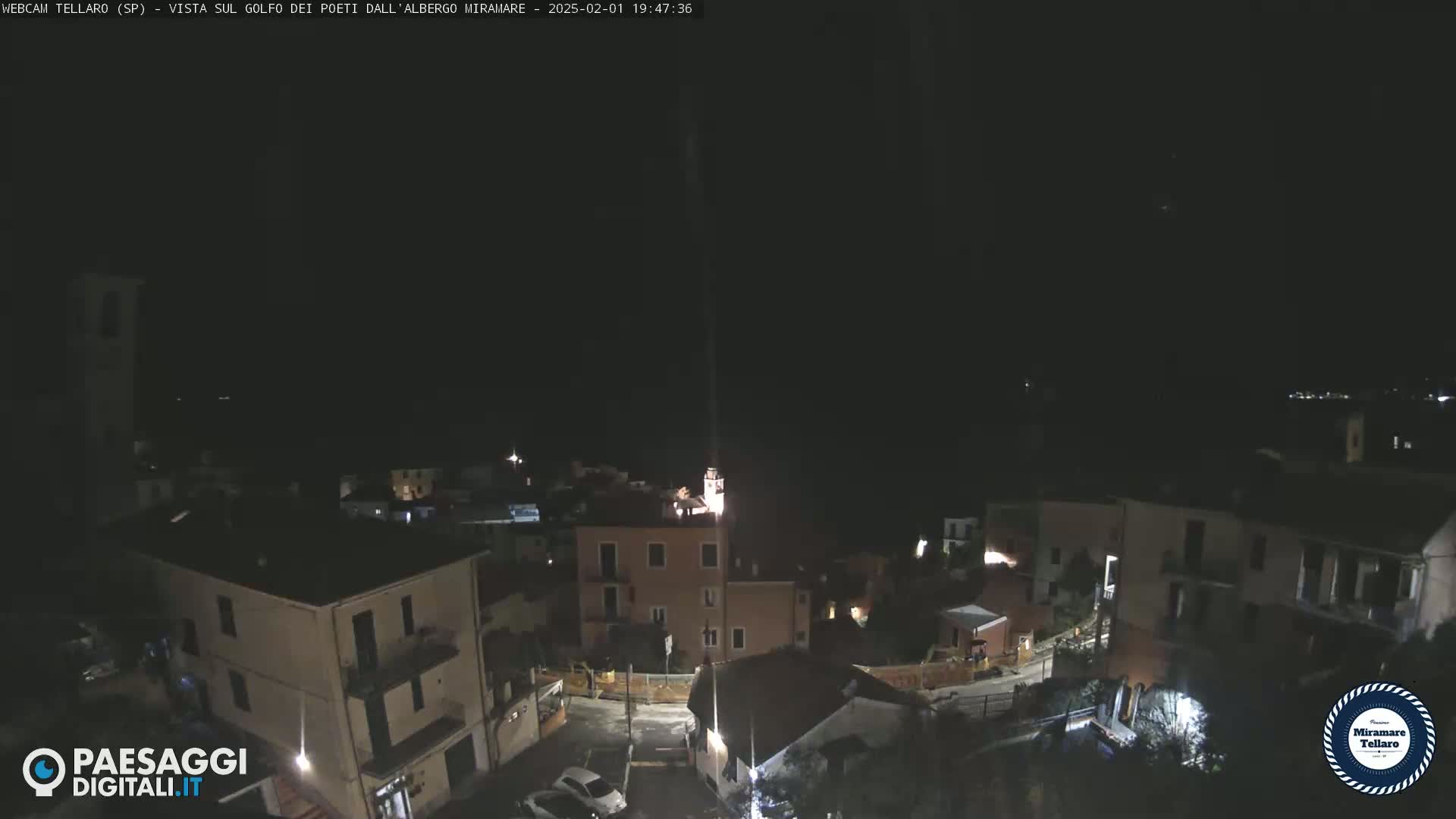 A nighttime, high-angle view of a small town nestled against a dark hillside, under a clear, dark sky.