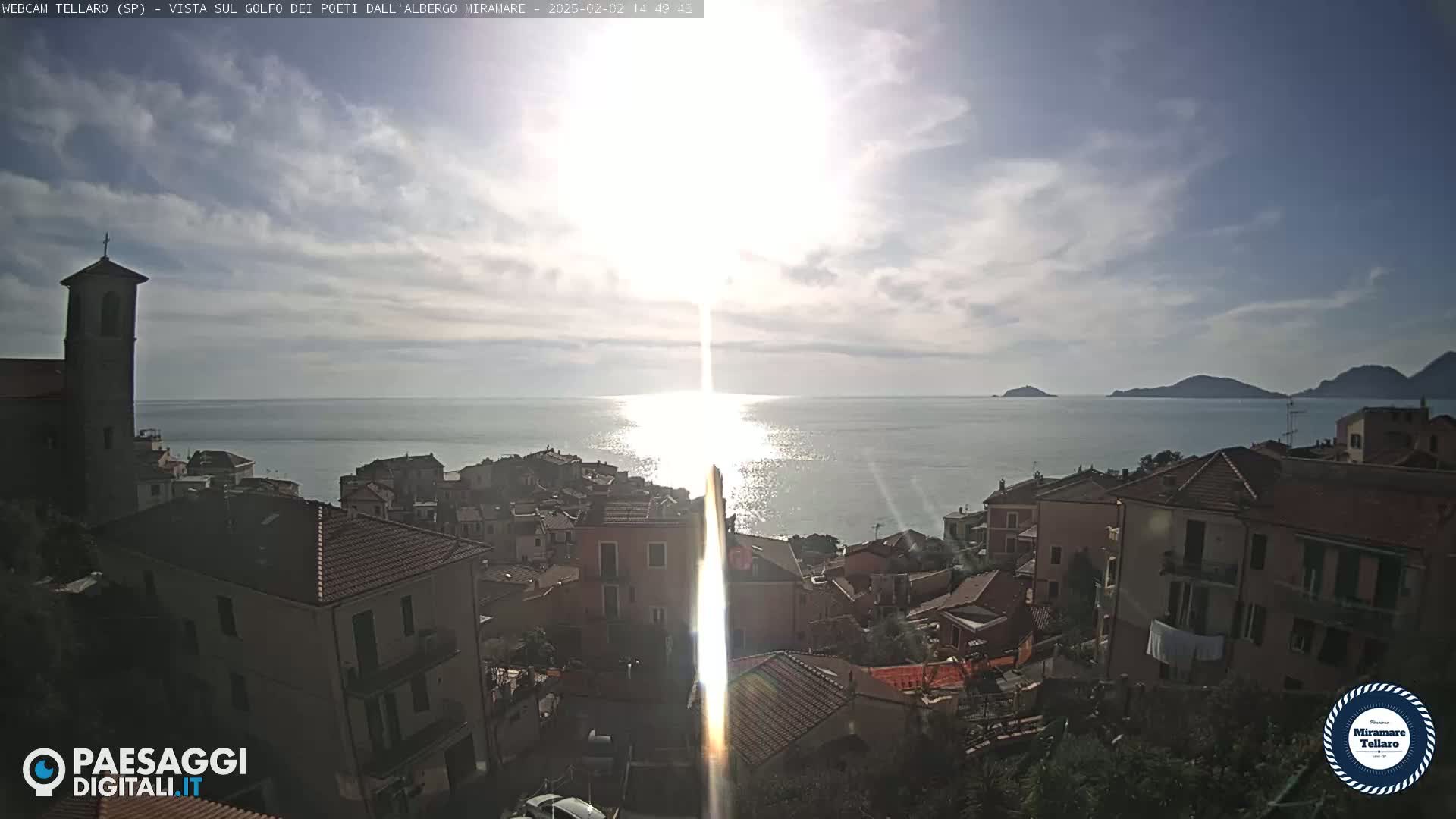 A coastal town with red-tiled roofs overlooks a calm sea under a partly sunny sky.
