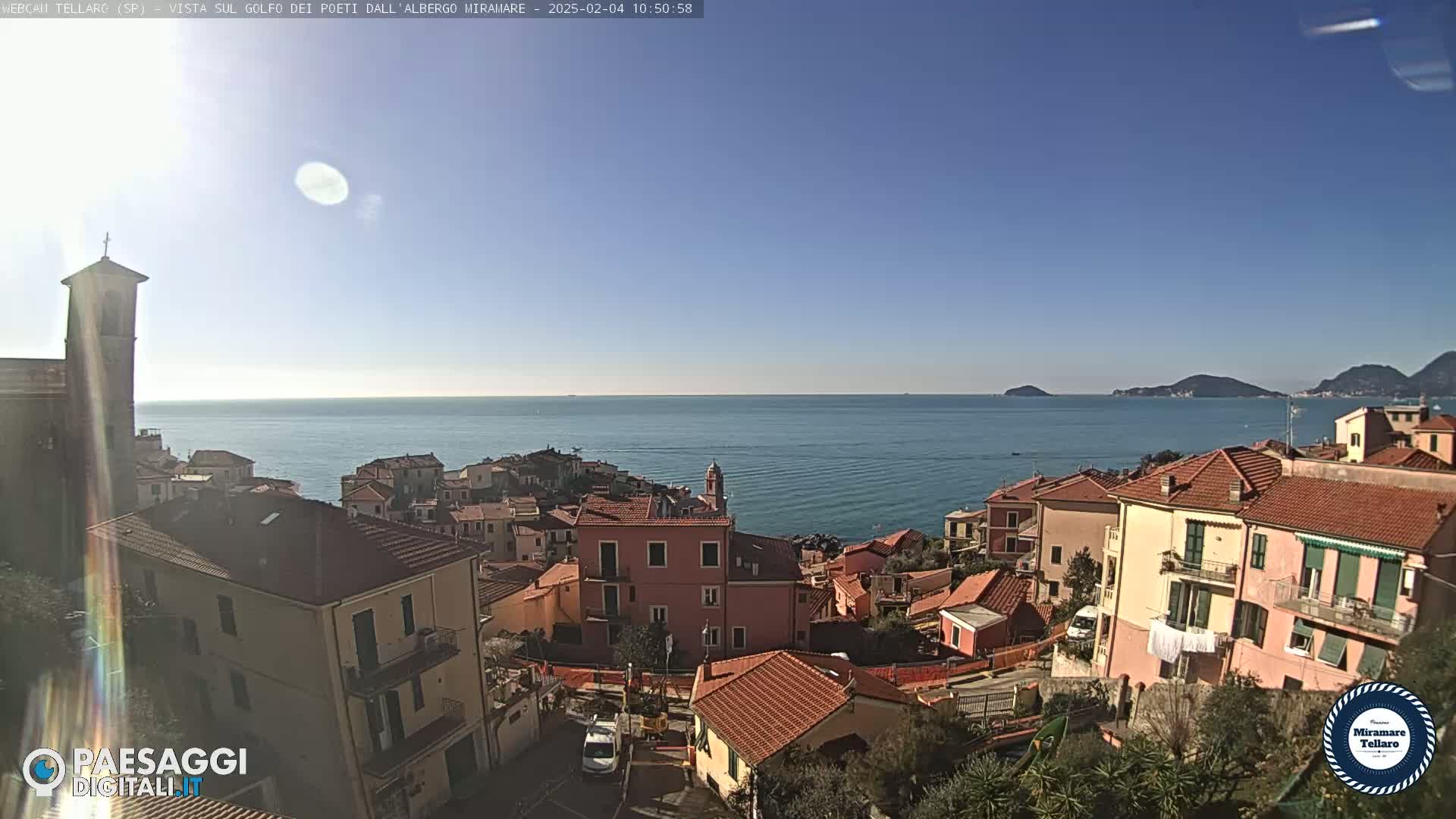 A coastal town with red-tiled roofs overlooks a calm sea under a clear blue sky.