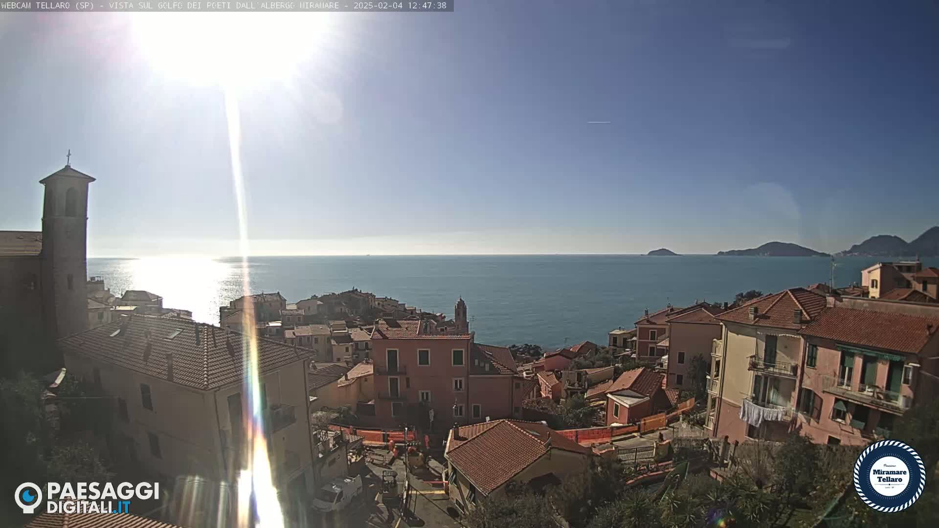 A coastal town with red-tiled roofs overlooks a calm, blue sea under a clear, sunny sky.