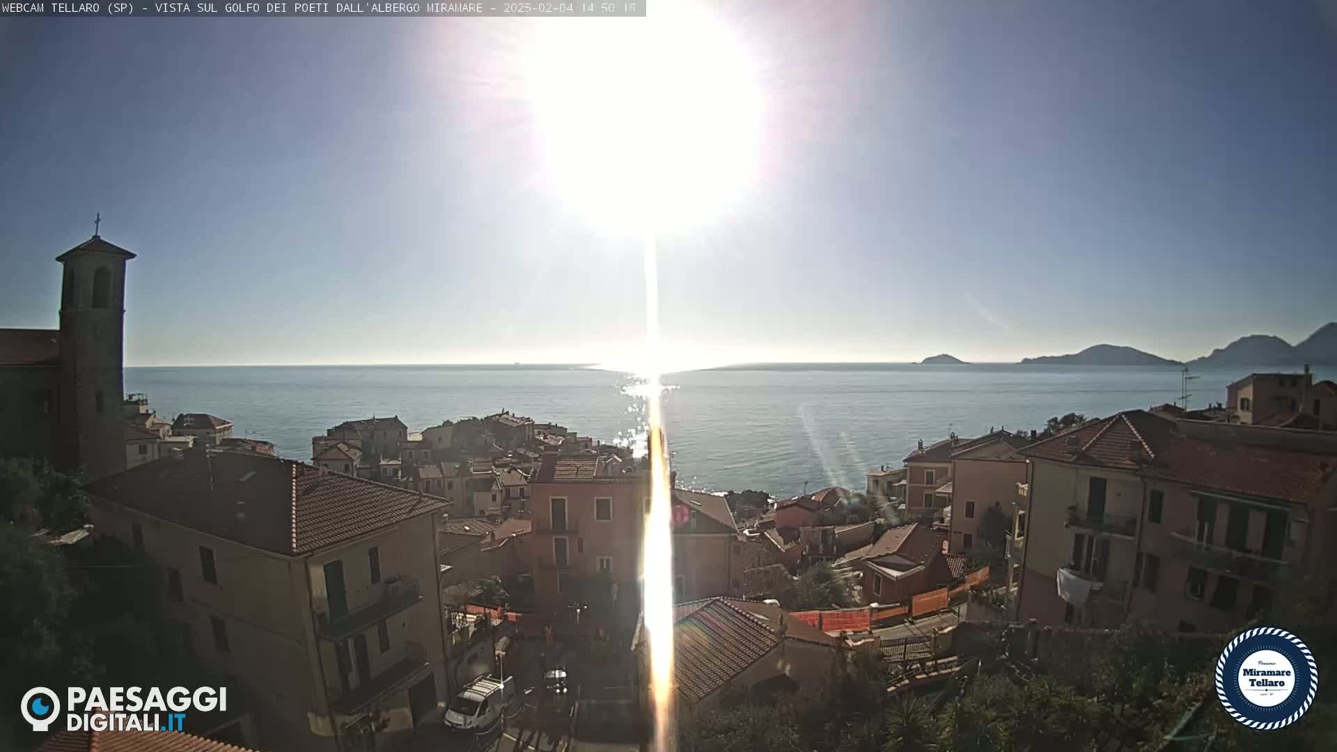 A coastal town with red-tiled roofs overlooks a calm sea under a bright, sunny sky.