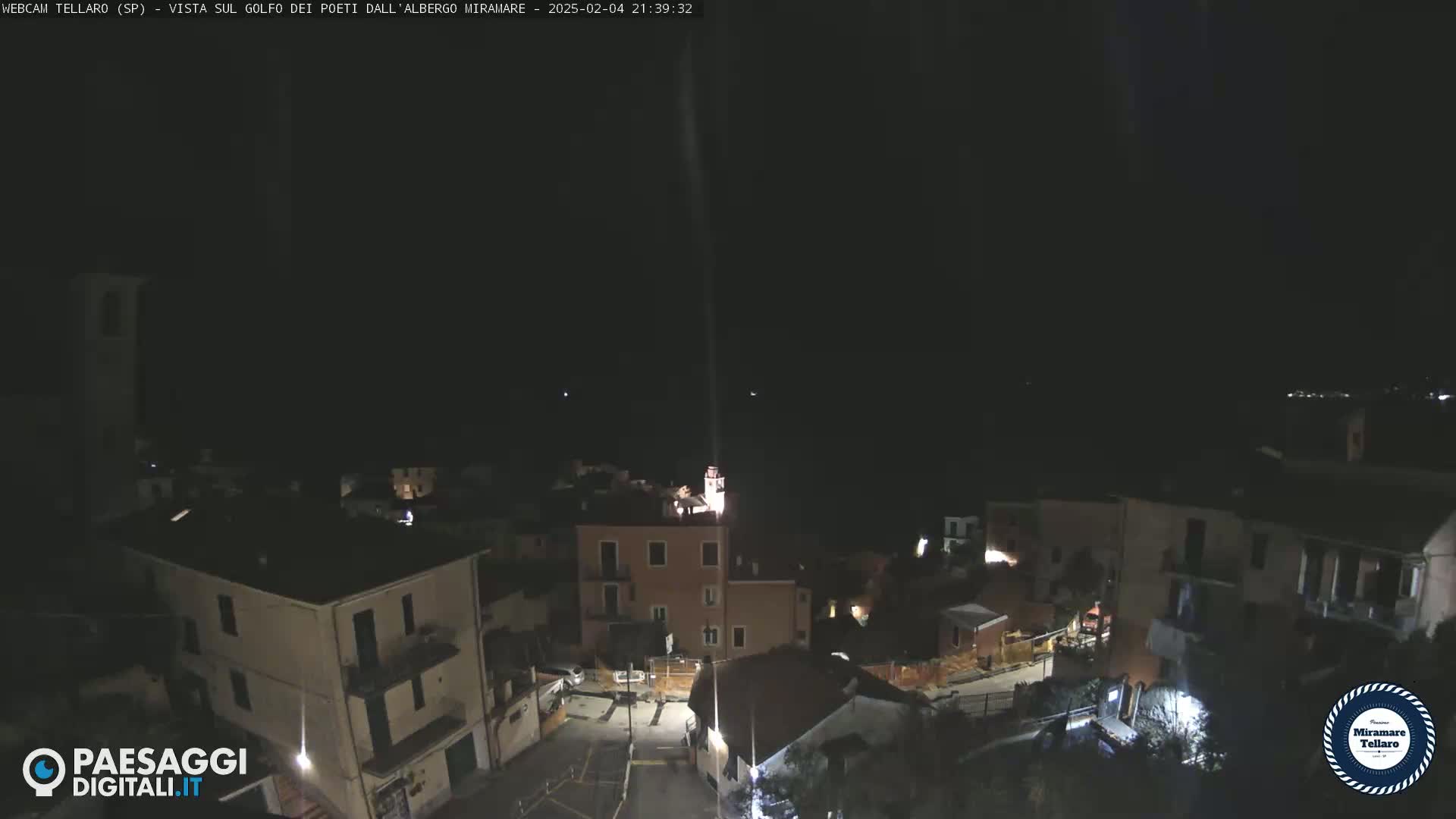 A nighttime view of a small town nestled on a hillside, with some lights illuminating buildings and streets under a dark, clear sky.