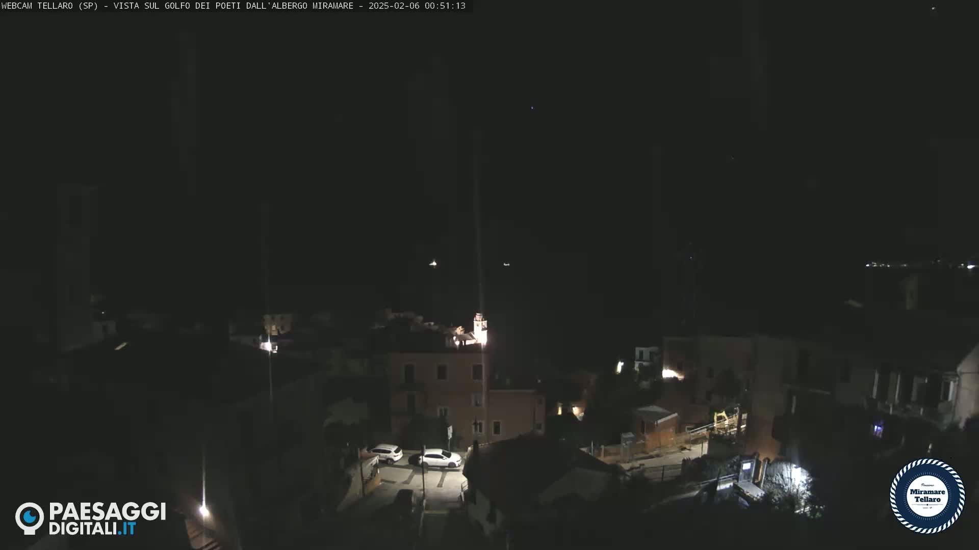 A nighttime view of a small town with a few illuminated buildings and cars parked on a street under a clear, dark sky.