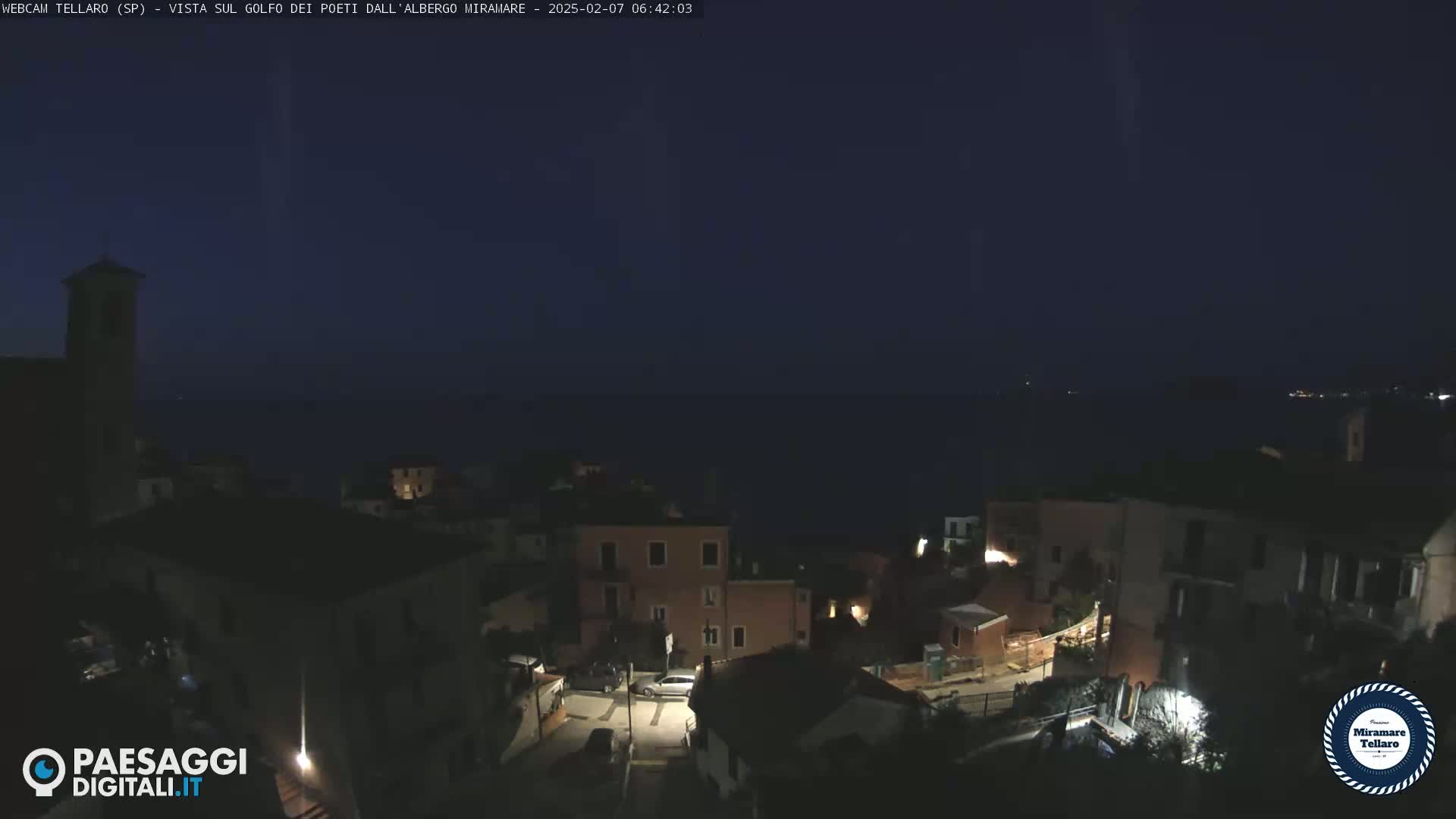 A nighttime view of a coastal town overlooking a dark sea under a clear, dark sky.