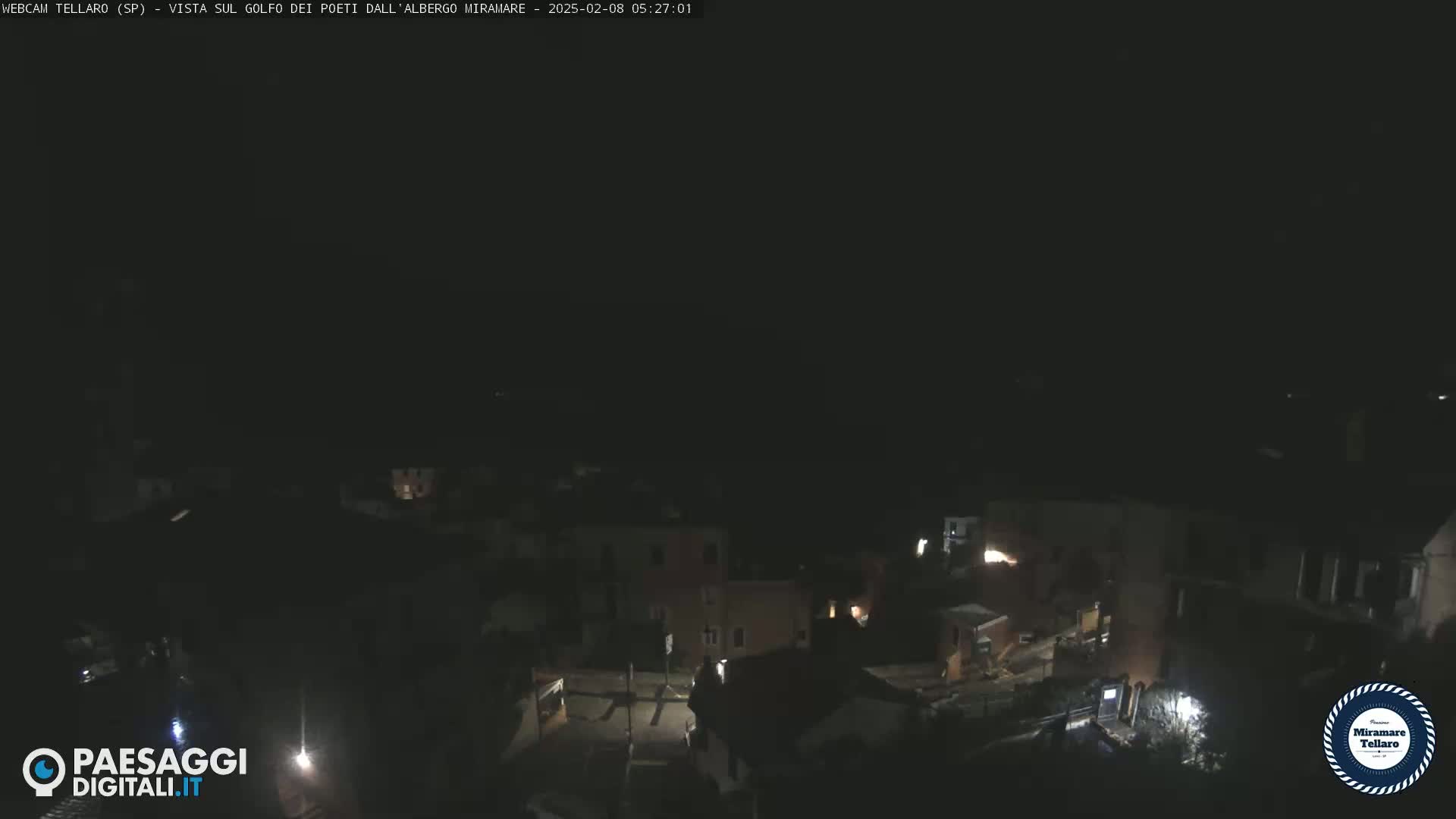A nighttime, overhead view of a dimly lit town with a few lights visible.