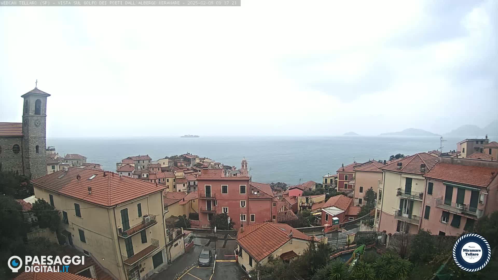 A coastal town with red-tiled roofs overlooks a calm sea under an overcast sky.