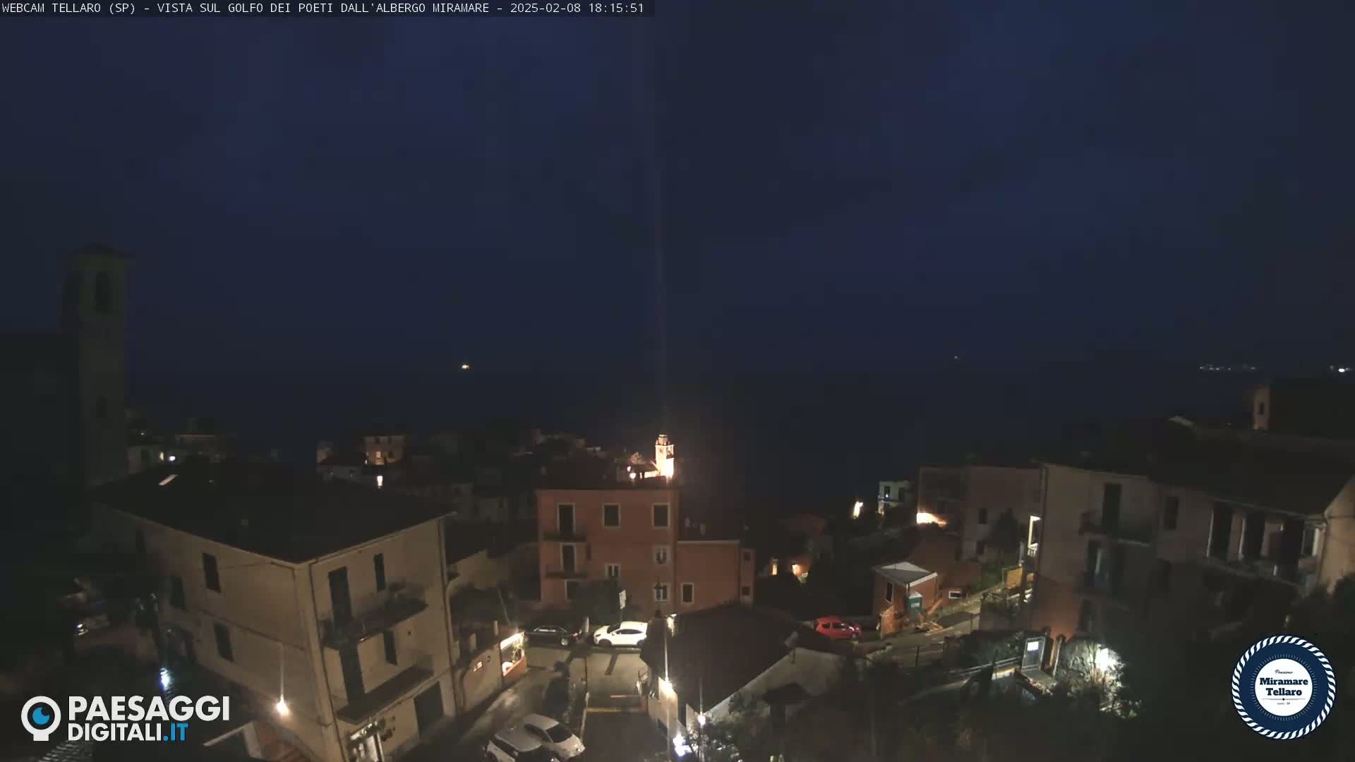 A nighttime view of a coastal town with a dark ocean in the background under a clear, dark sky.