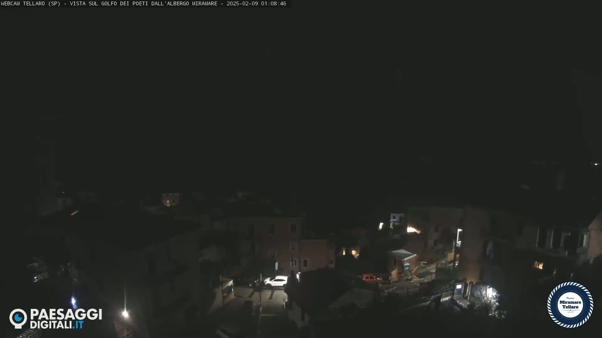 A nighttime, high-angle view of a dark village with a few illuminated buildings and vehicles.