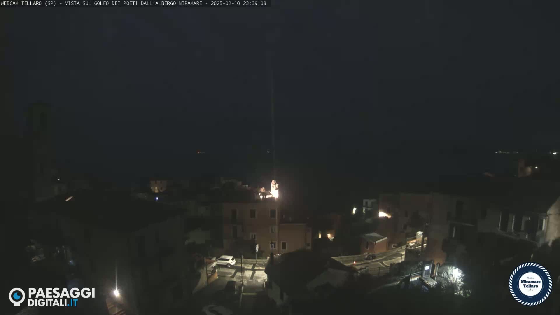 A nighttime view of a coastal town with a dark sky and sparsely lit buildings near the water.