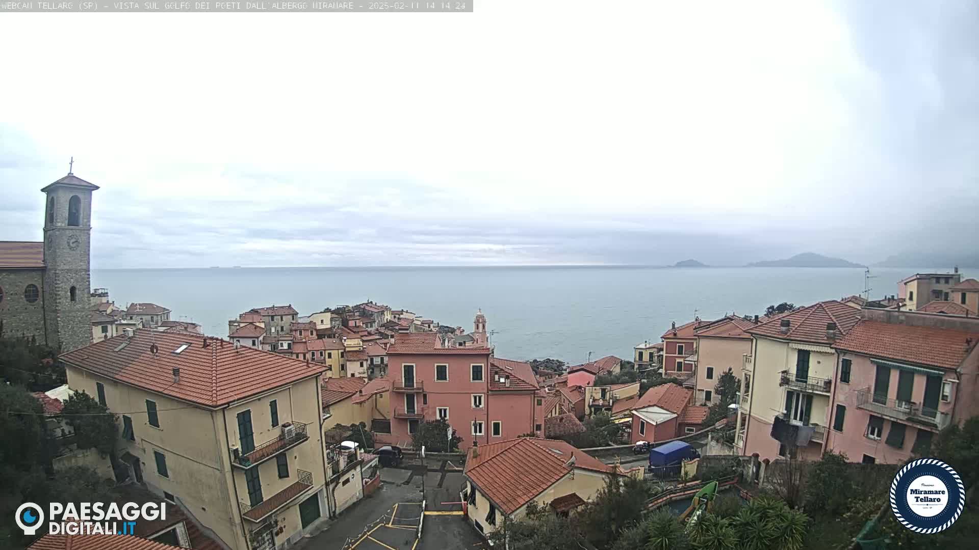 A coastal town with red-tiled roofs overlooks a calm sea under an overcast sky.