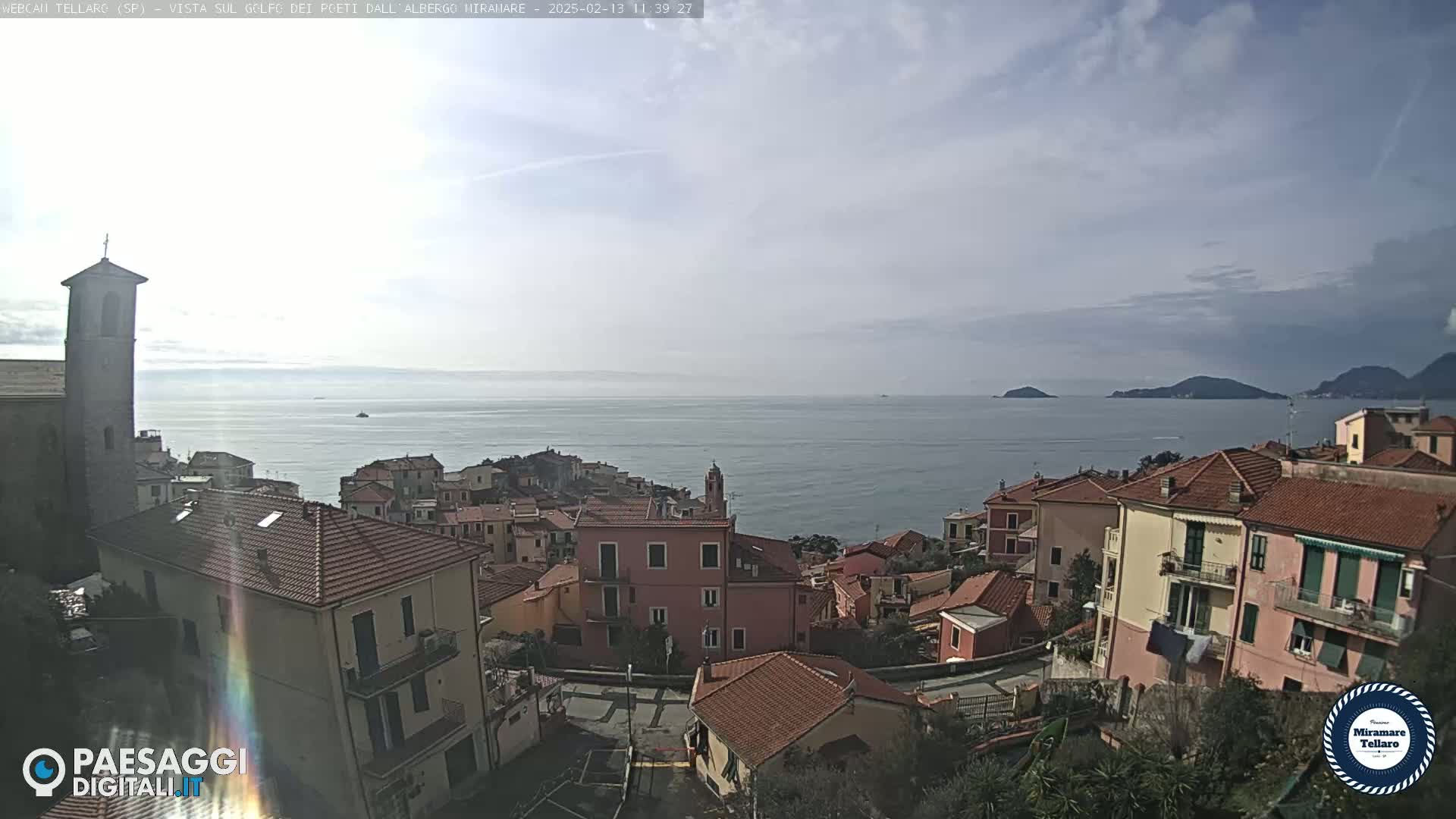 A coastal town with red-tiled roofs overlooks a calm sea under a mostly cloudy sky.