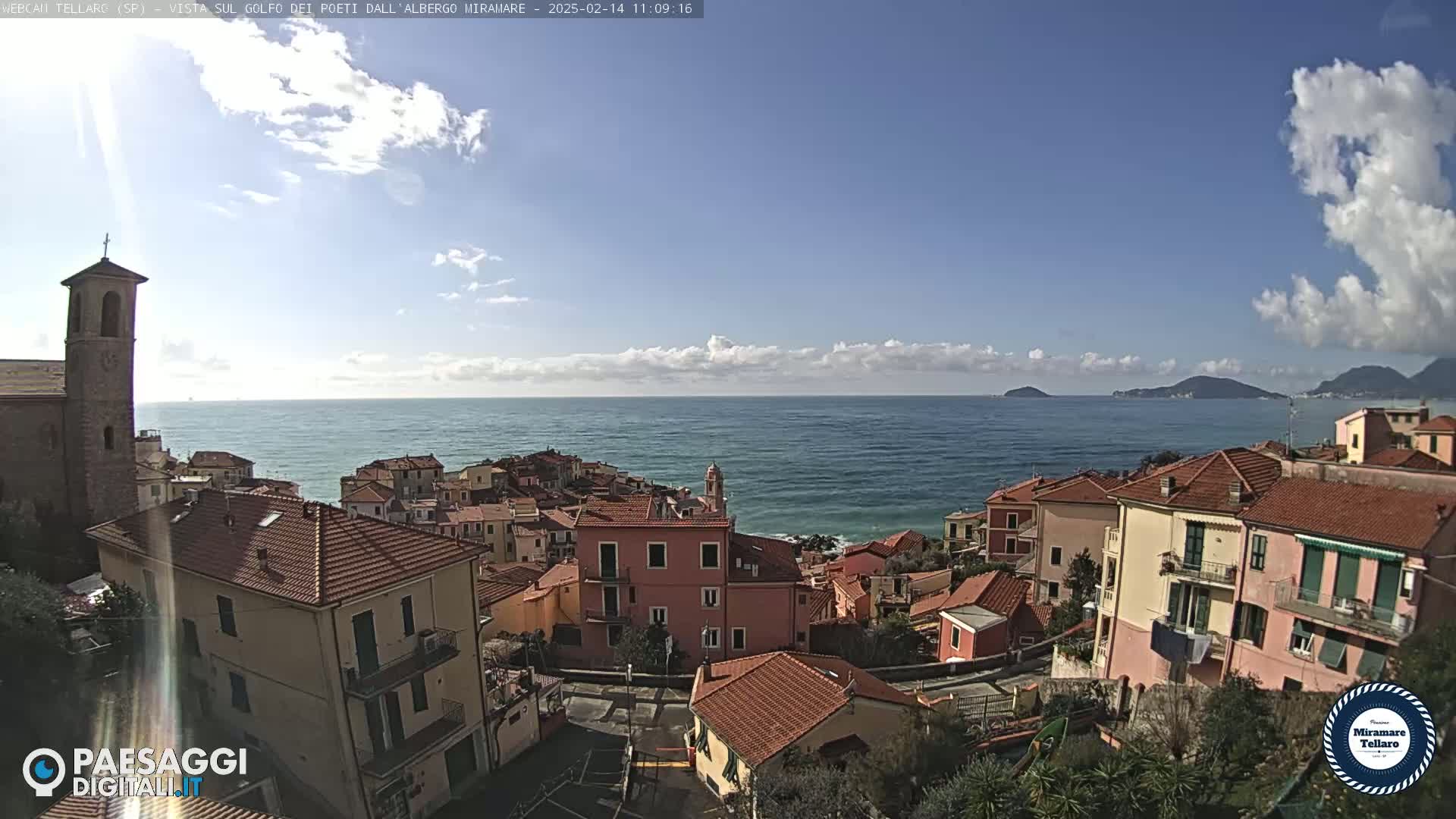 A coastal town with red-tiled rooftops overlooks a calm sea under a partly cloudy sky.