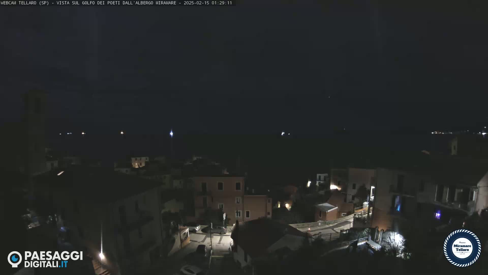 A nighttime, dark view of a coastal town with a few lights visible, overlooking a dark body of water.