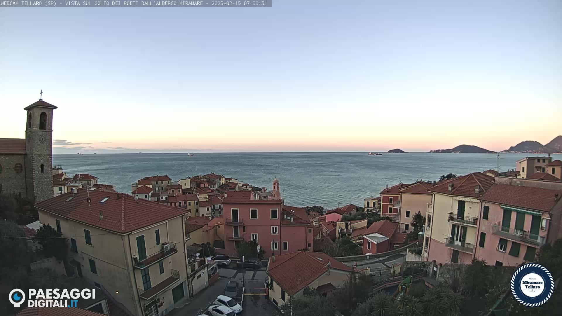 A coastal town with red-roofed buildings overlooks a calm sea under a clear, twilight sky.