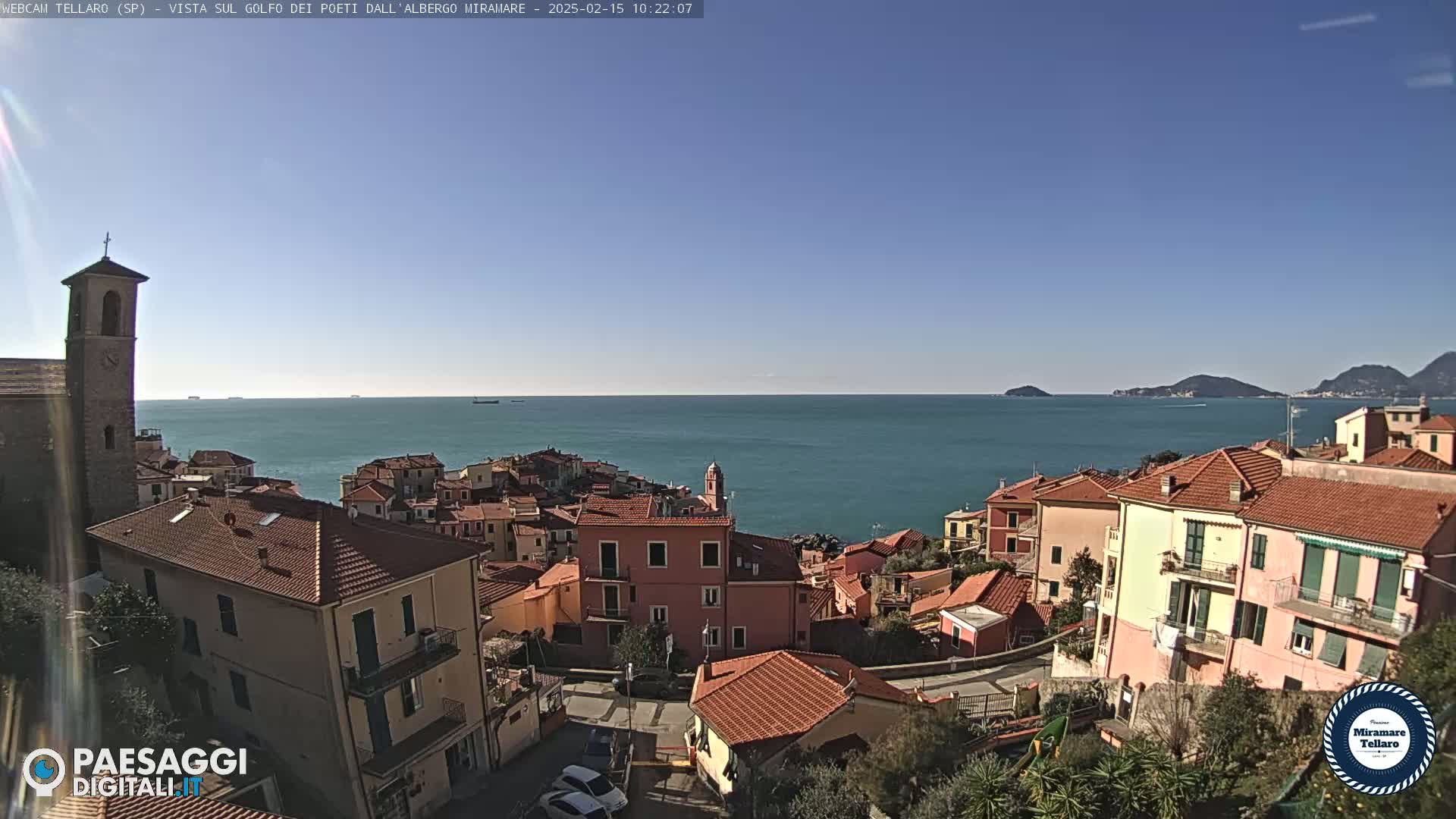 A coastal town with red-tiled roofs overlooks a calm blue sea under a clear blue sky.