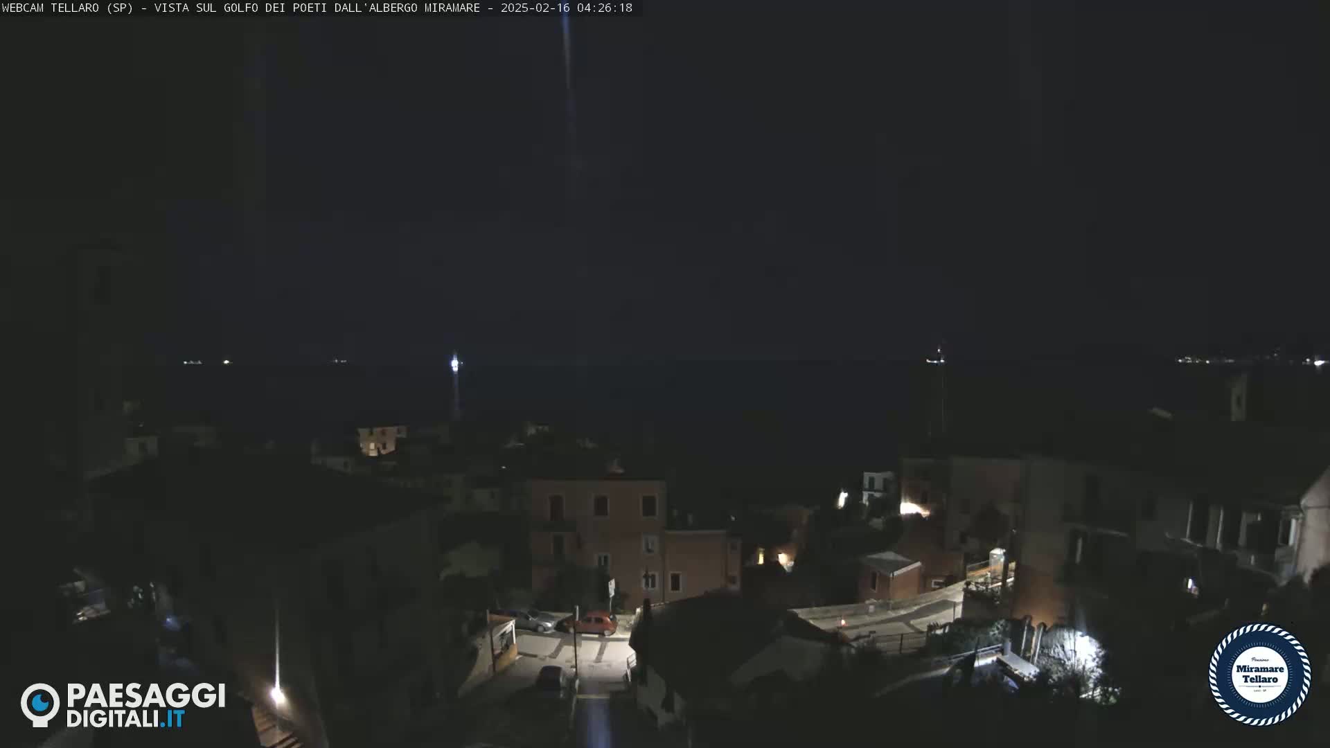 A nighttime view of a coastal town, with dimly lit buildings and a dark sea under a clear sky.