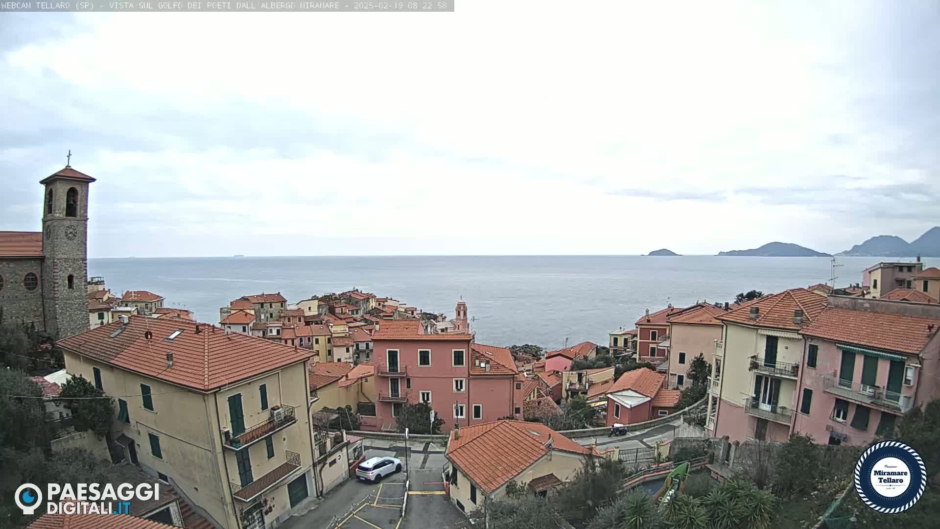 A coastal village with red-tiled roofs overlooks a calm sea under an overcast sky.
