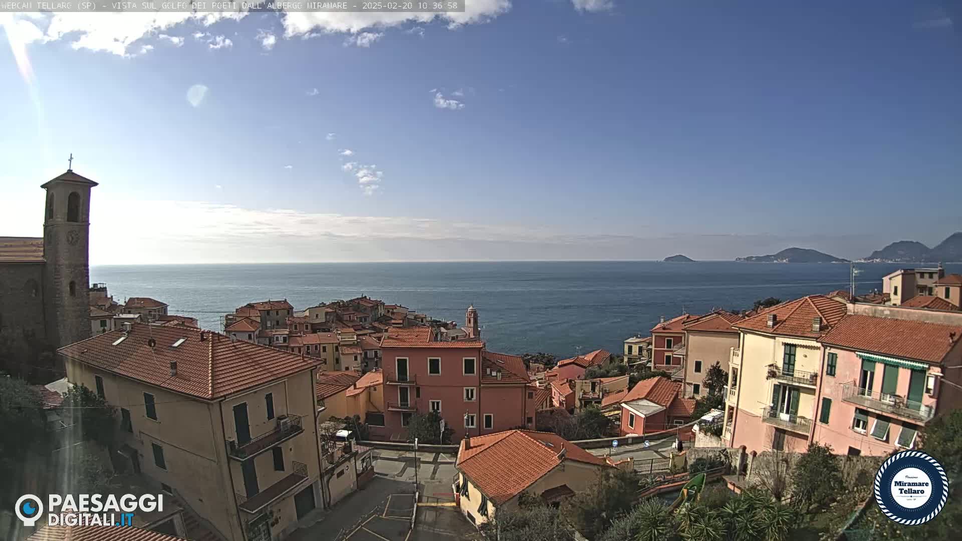 A coastal town with red-tiled roofs overlooks a calm sea under a mostly clear sky.