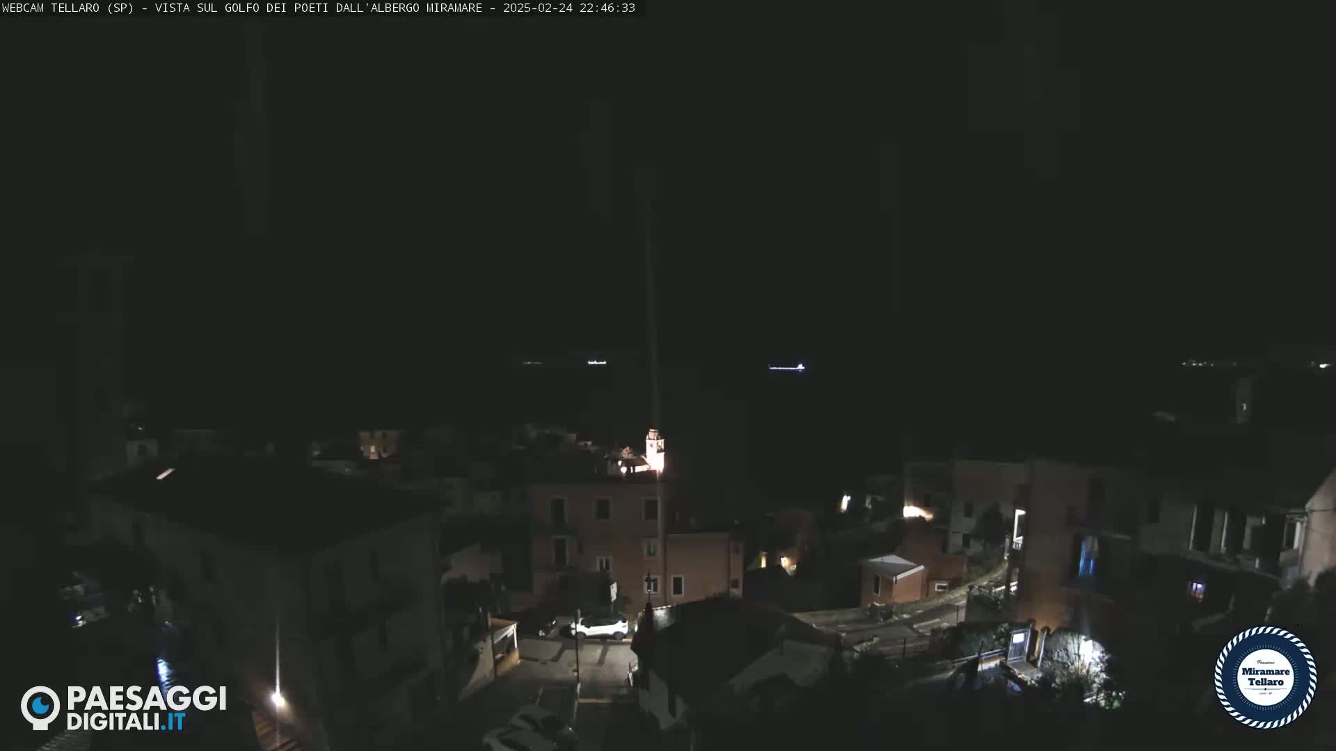A nighttime, high-angle view of a coastal town, with a dark sea visible in the background.