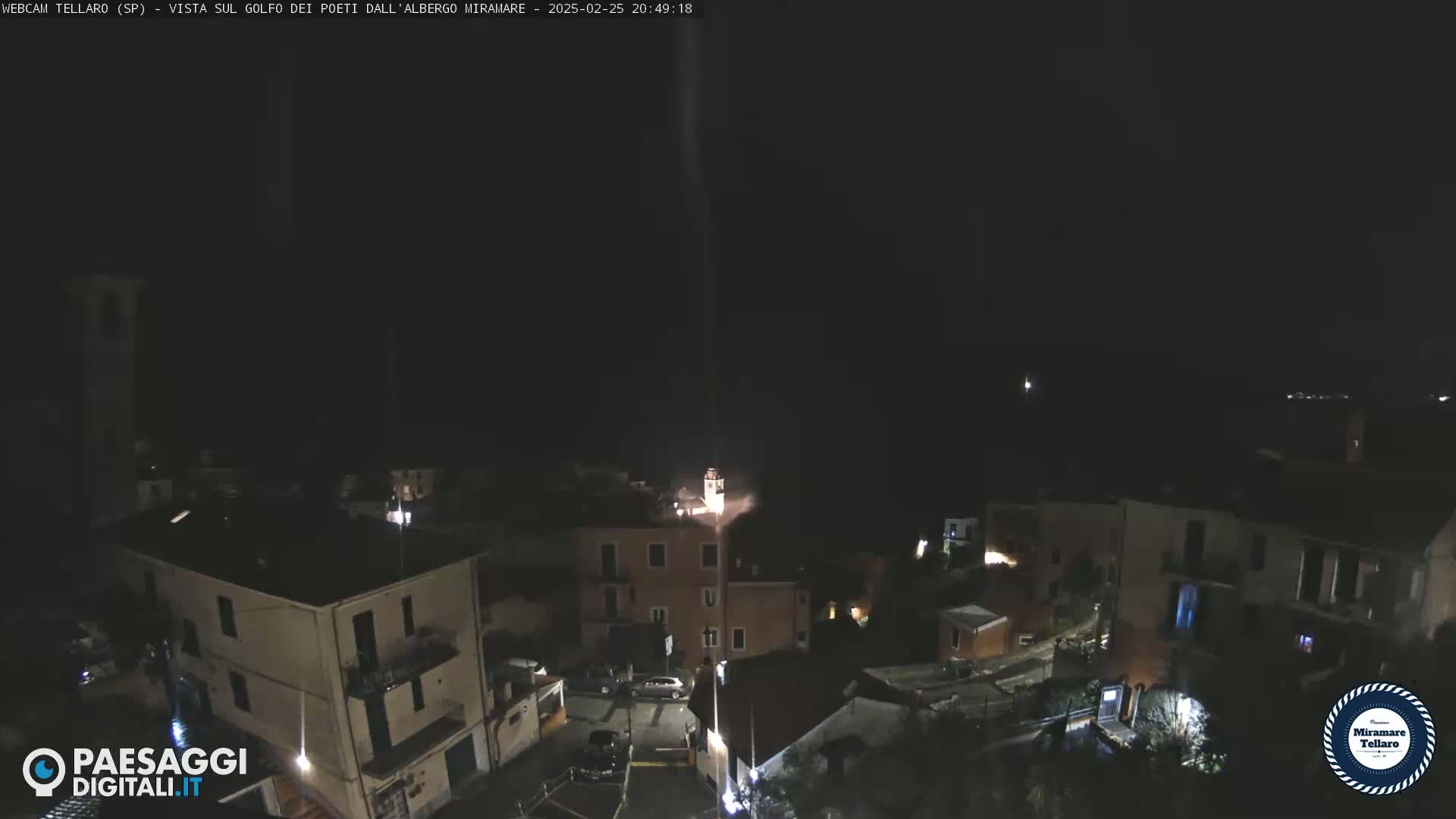 A nighttime, overhead view of a small town nestled on a hillside, with a few lights visible on buildings and streets.