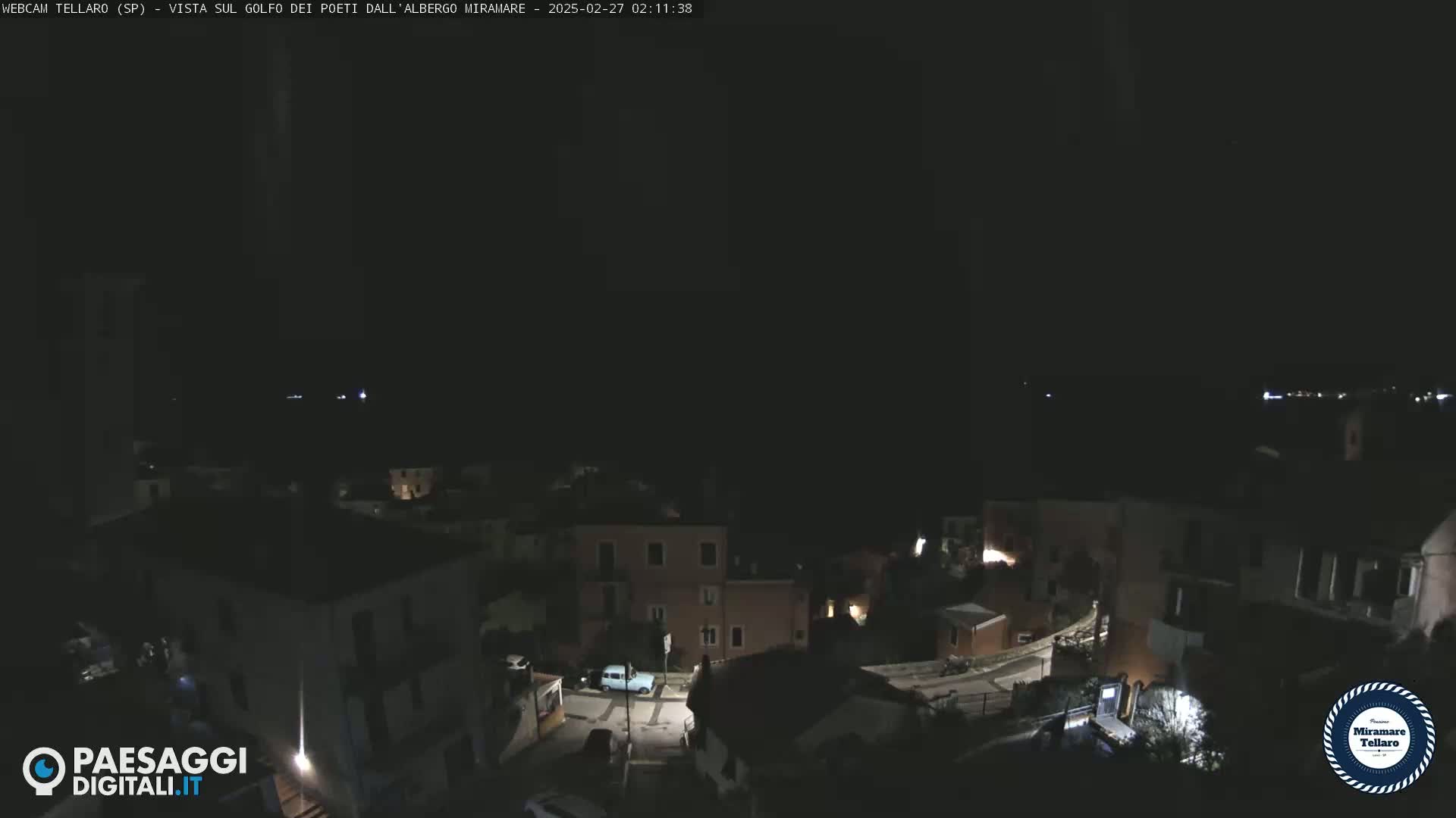 A nighttime, aerial view of a small town situated on a hill overlooking a dark body of water.