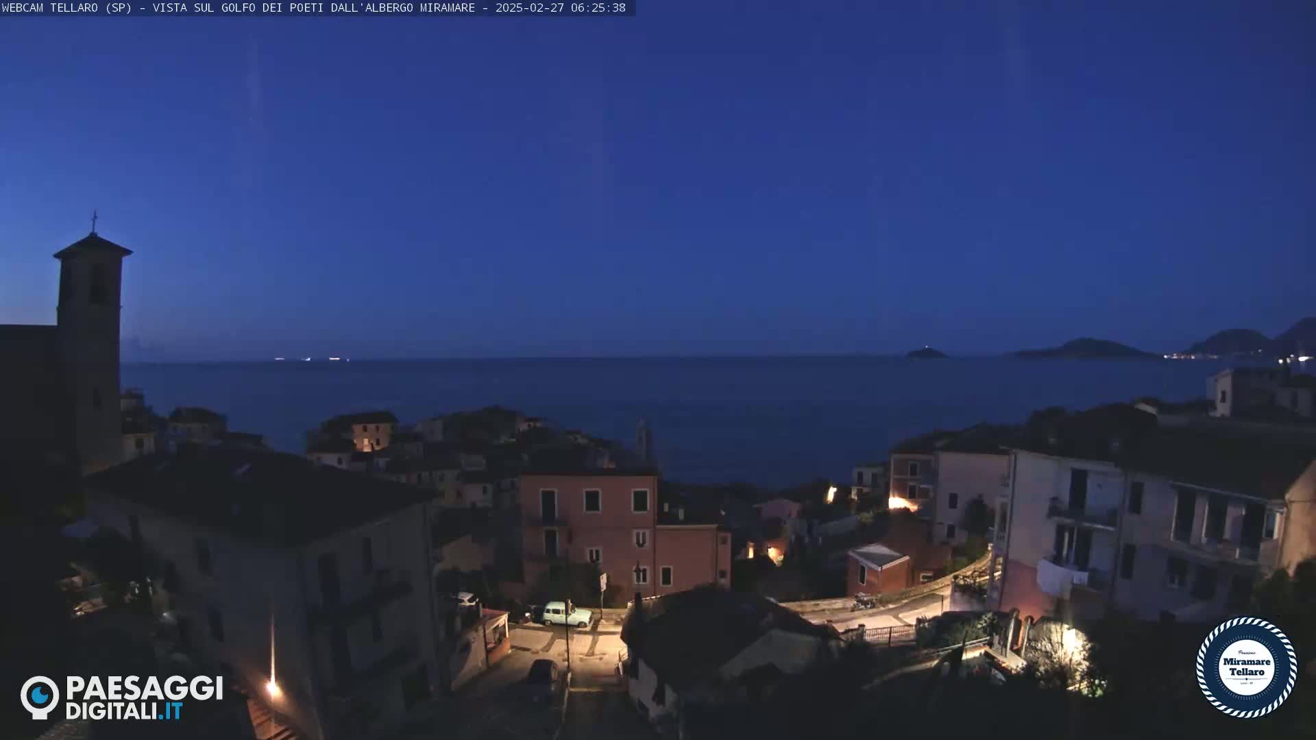 A coastal town at twilight, with a church steeple visible, overlooks a dark blue sea under a clear, night sky.