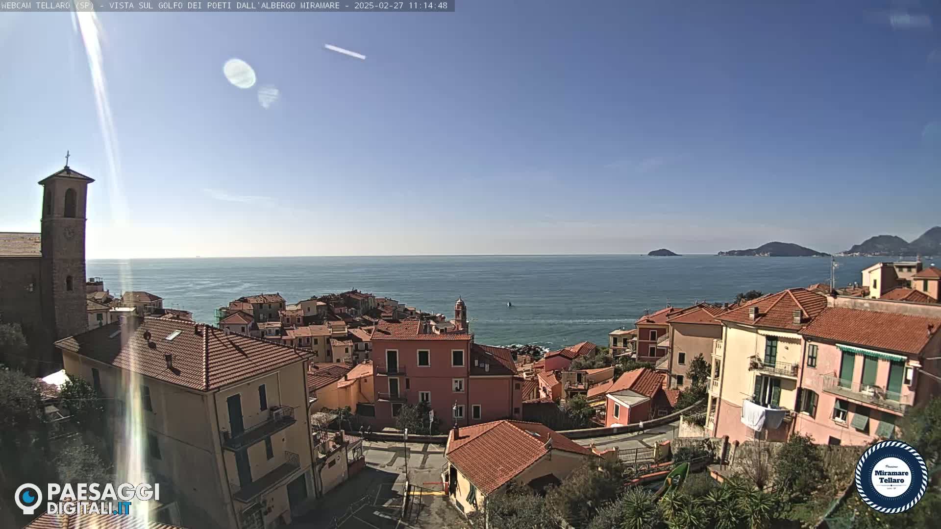 A coastal town with red-tiled roofs overlooks a calm blue sea under a clear sky.